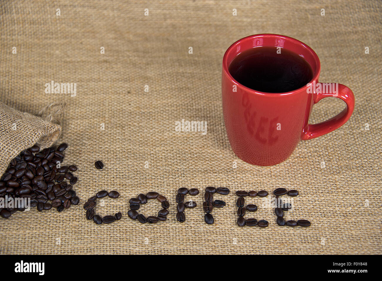 Rohe Kaffeebohnen auf Sackleinen mit rote Kaffeetasse. Stockfoto