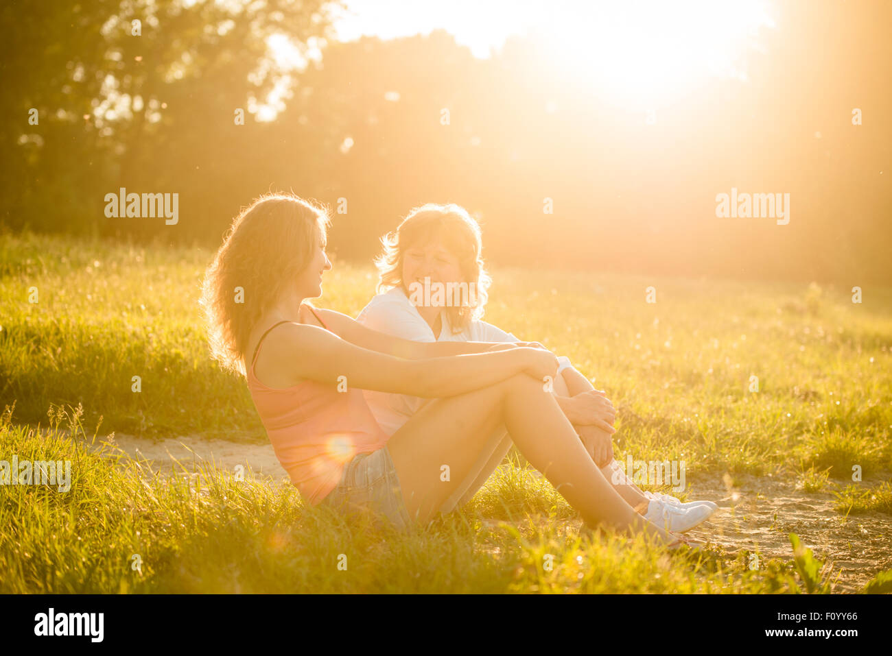 Teenager-Mädchen sprechen mit ihrer Mutter sitzen auf dem Rasen in der Natur, Fackel aus untergehende Sonne auf Foto Stockfoto