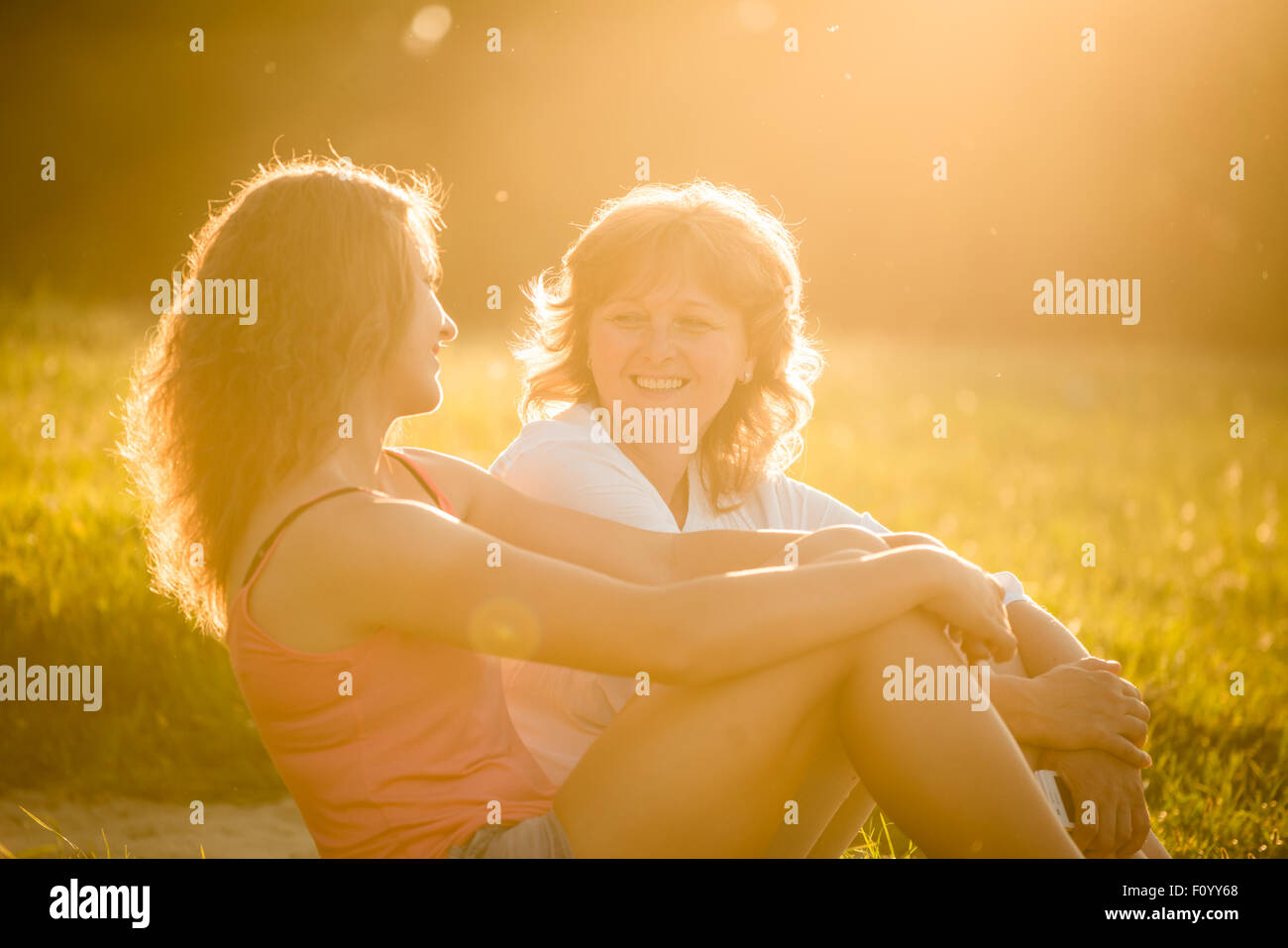 Teenager-Mädchen sprechen mit ihrer Mutter sitzen auf dem Rasen in der Natur, Fackel aus untergehende Sonne auf Foto Stockfoto