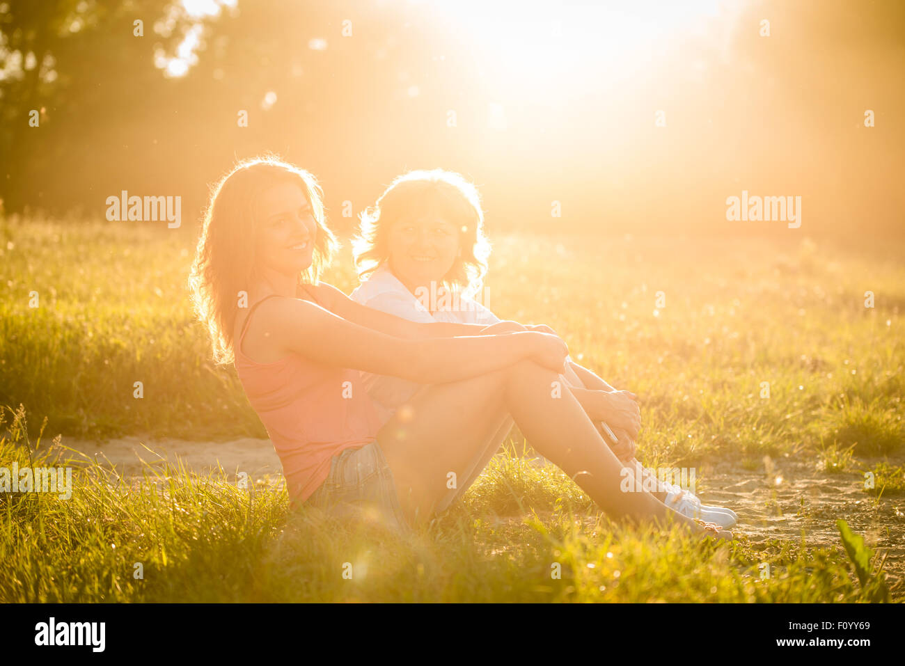 Teenager-Mädchen h Mutter sitzen auf dem Rasen in der Natur, Fackel aus untergehende Sonne auf Foto Stockfoto