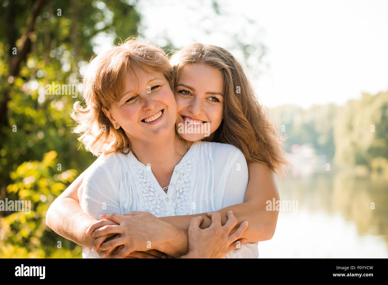 Reife Mutter umarmt mit Teen Tochter in der Natur im Freien an sonnigen Tag Stockfoto