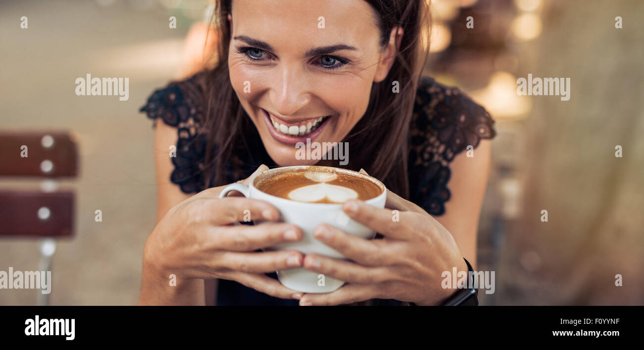 Schuss der fröhliche junge Frau trinken Kaffee in einem Café und wegsehen hautnah. Kaukasischen Frauen bei einer Tasse Kaffee. Stockfoto
