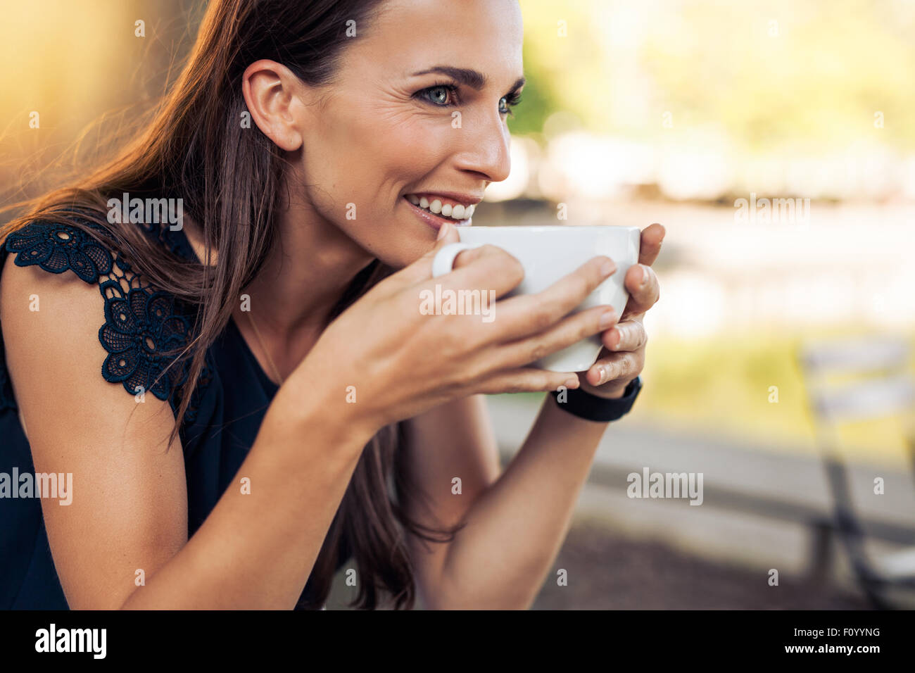 Junge Frau hält eine Tasse Kaffee und schauen weg Lächeln auf den Lippen. Kaukasischen Frauen trinken Kaffee im Café. Stockfoto