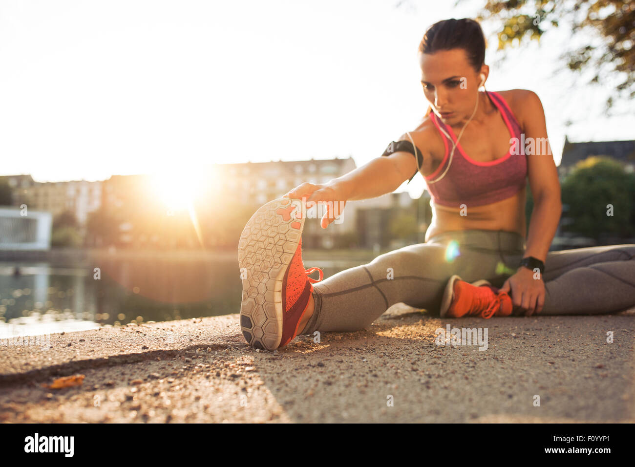 Fitness-Frau vor einem Lauf dehnen. Junge weibliche Läufer dehnen Sie ihre Muskeln vor einer Trainingseinheit. Sie sitzt auf s Stockfoto