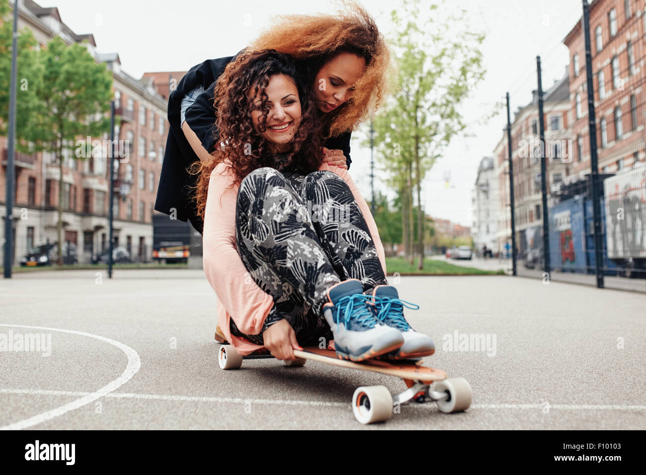 Glückliche junge Frauen eine Menge Spaß, Reiten zusammen auf Skateboard.  Frauen schieben ihre Freundin sitzt auf einem langen Brett - Outdoor  Stockfotografie - Alamy