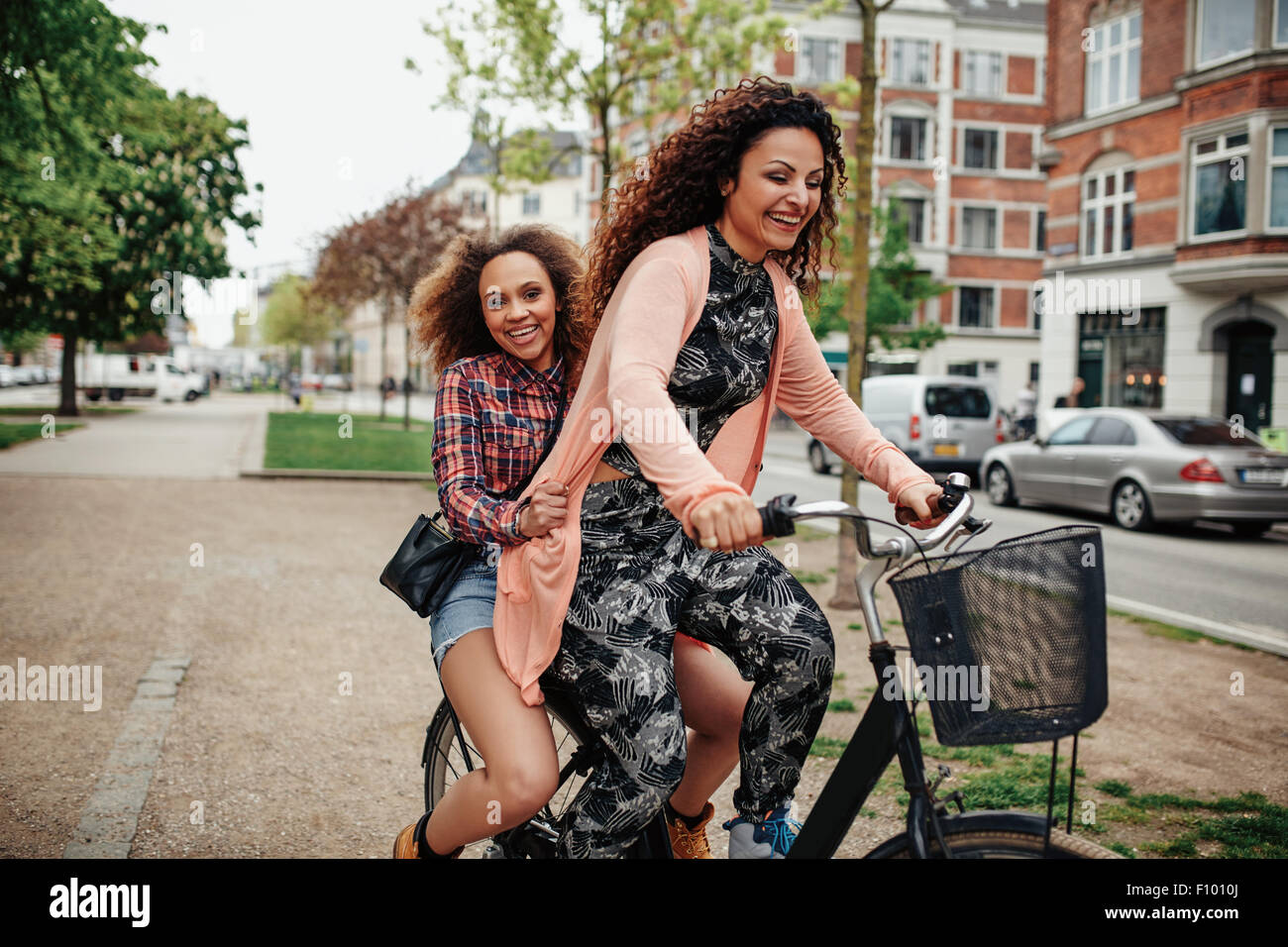Fröhliche junge Frauen genießen Fahrrad fahren auf Stadtstraße. Zwei junge Mädchen zusammen reiten auf einem Fahrrad. Stockfoto
