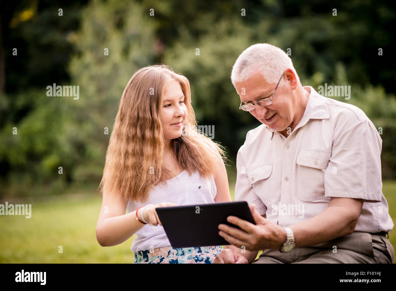 Ältere Mann mit seinem Enkel suchen gemeinsam auf Fotos in Smartphone - draußen in der Natur Stockfoto