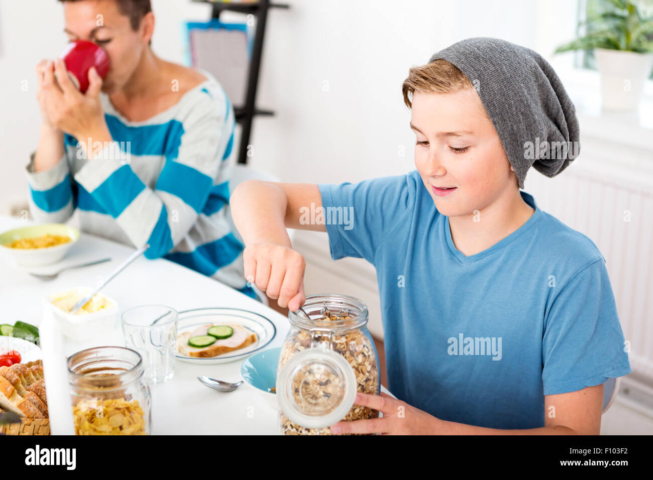 Mutter und Sohn zusammen mit Frühstück am Morgen. Sohn mit Getreide aus einer Flasche am Frühstückstisch. Stockfoto