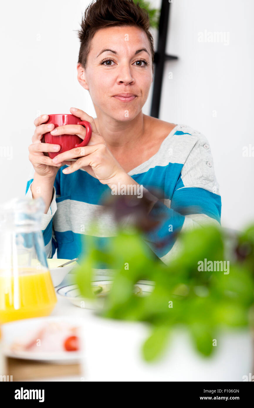 Frau sitzt am Frühstückstisch hält eine Kaffeetasse in ihr beide Hände. Stockfoto