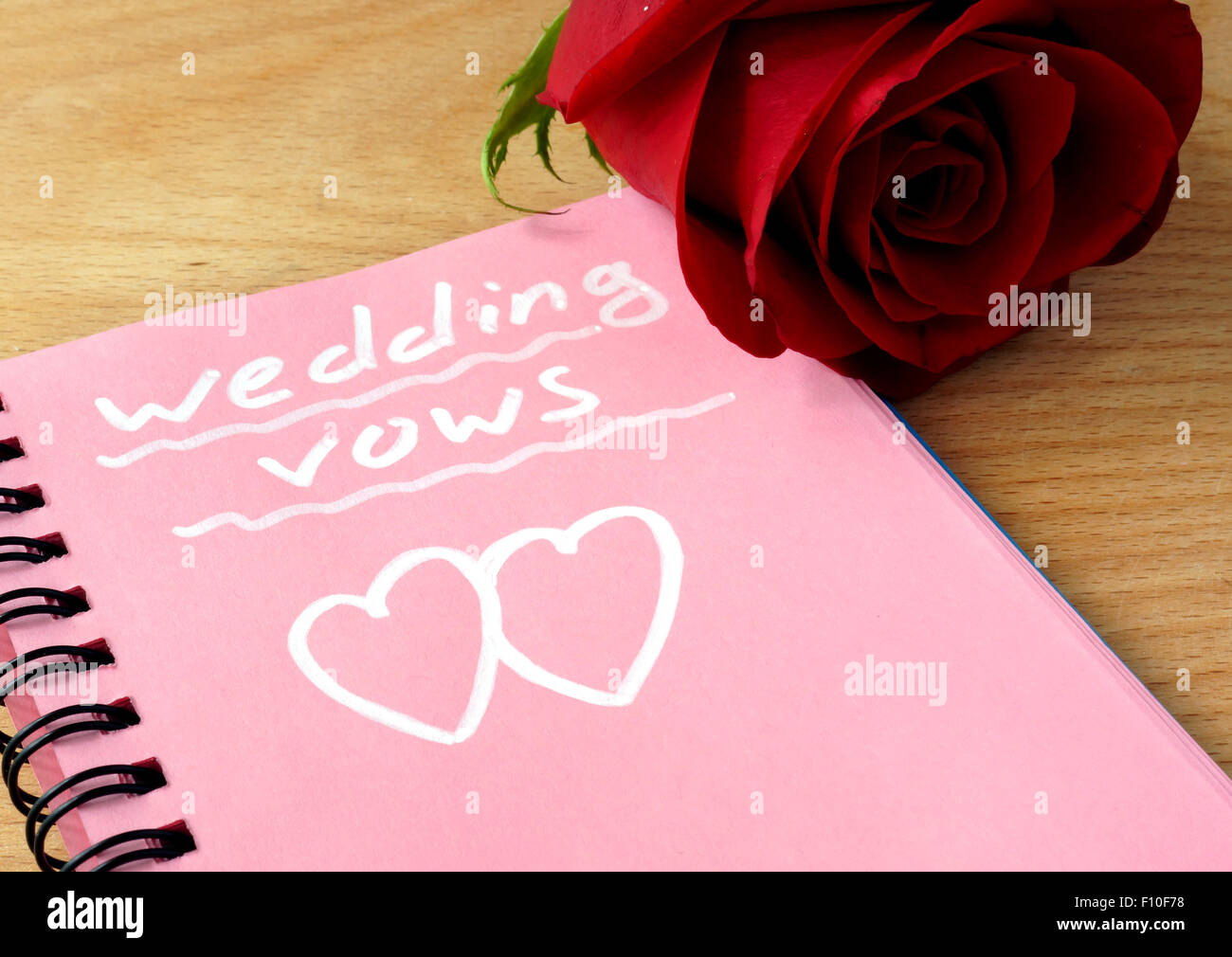 Rosa Notizblock mit Eheversprechen und Rose auf einem hölzernen Hintergrund. Stockfoto