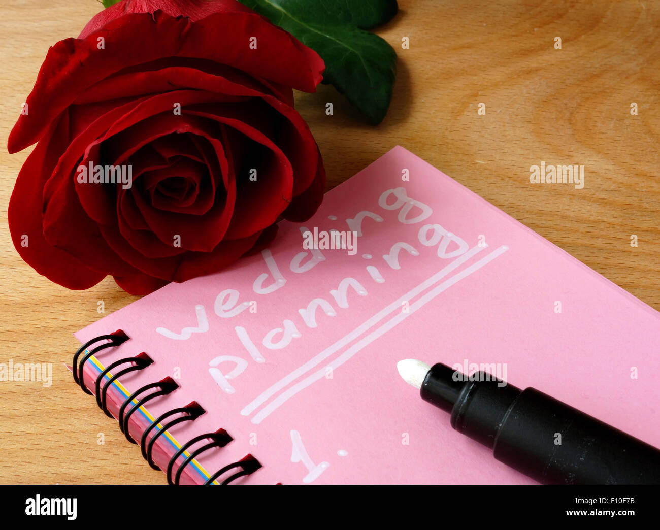 Rosa Notizblock mit Hochzeitsplanung und Rose auf einem hölzernen Hintergrund. Stockfoto