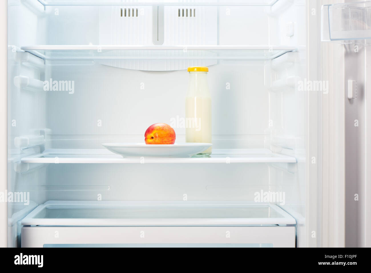 Zweifarbig Orange und rot auf weißem Teller und eine Glasflasche Joghurt in offenen leeren Kühlschrank Pfirsich. Gewicht-Verlust-Diät-Konzeptionierung Stockfoto