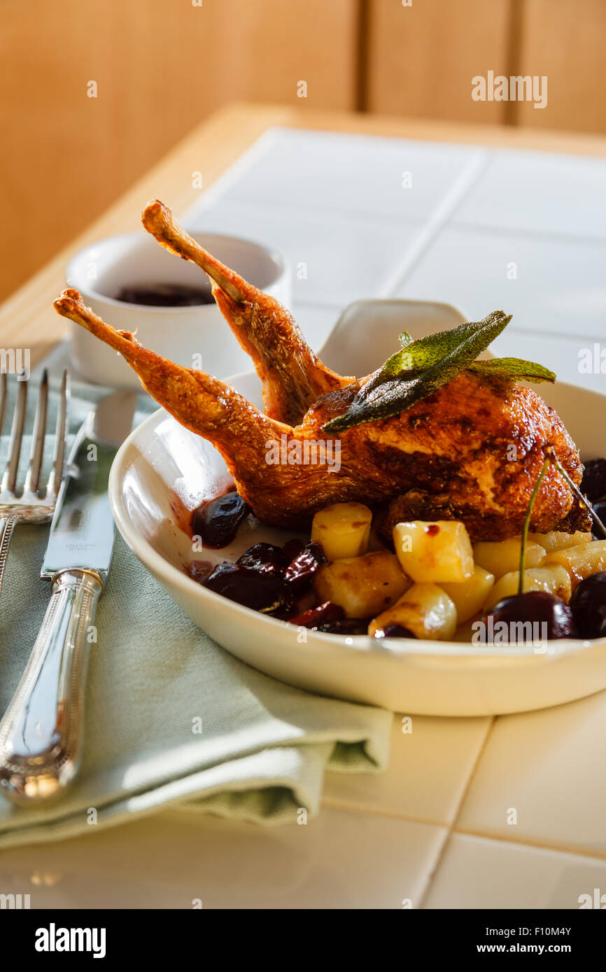 Gebratene Wachtel mit Kirsche & brandy Sauce & Fondant Kartoffelwürfel in weiße Schale mit traditionellen Silberbesteck auf Serviette serviert. Stockfoto