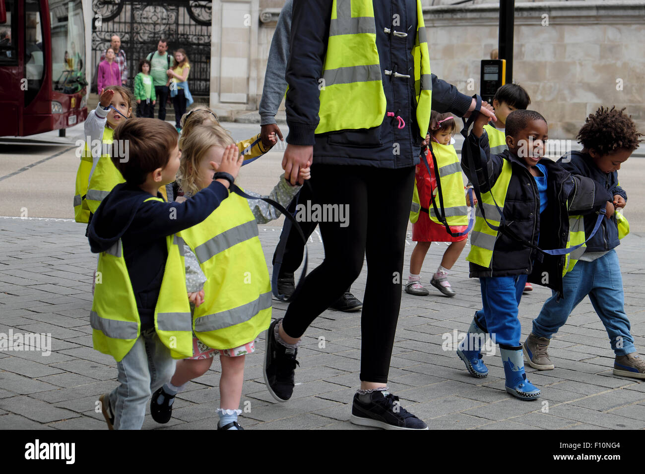 Kindergarten-Ausflug Kinder und Tagesmütter tragen gut sichtbare, gut sichtbare Sicherheitsjacken und halten ihre Hände auf Walk in Street in London, Großbritannien KATHY DEWITT Stockfoto