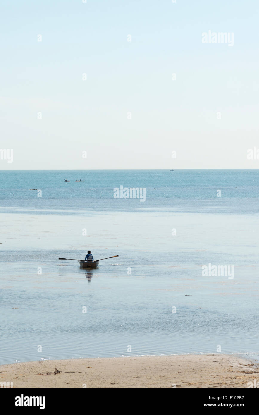 Eine Person, die ein kleines Ruderboot am Ufer Meeres bei Ebbe an Bembridge Isle Of Wight UK Stockfoto