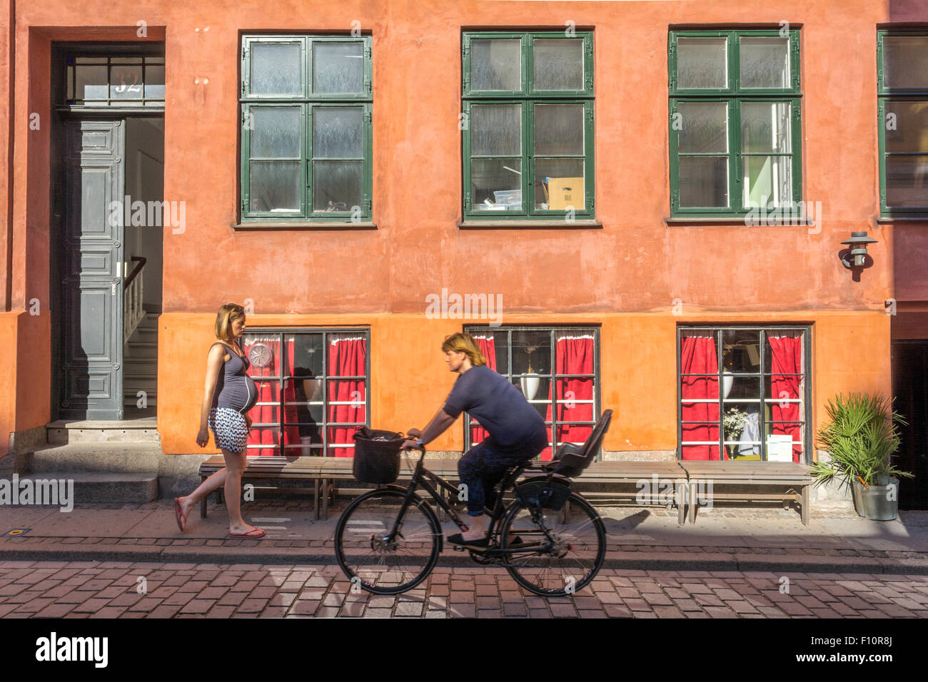 Eine schwangere Frau läuft in Kopenhagen in Dänemark auf einer farbenfrohen Kopfsteinpflasterstraße Stockfoto