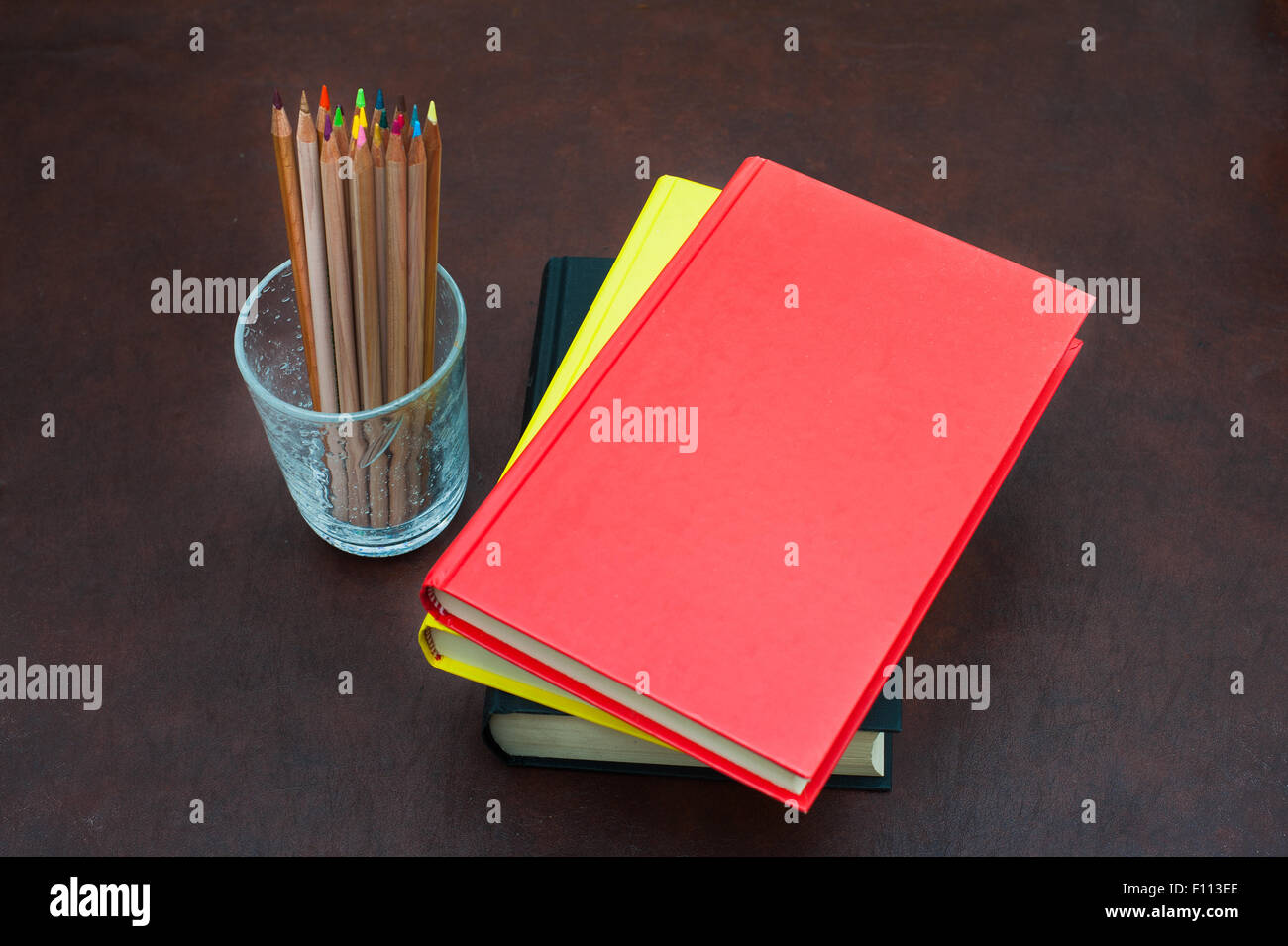 Buntstifte und Stapel Bücher mit rotem Einband auf hölzernen desktop Stockfoto