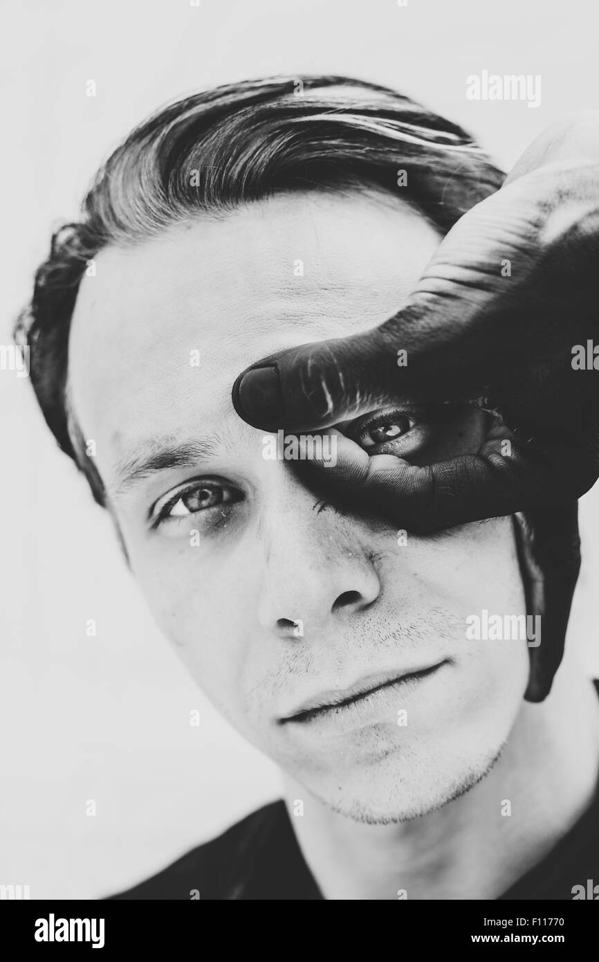 Schwarz-weiß-Porträt eines Mannes mit bemalten Fingern über dem Gesicht Stockfoto