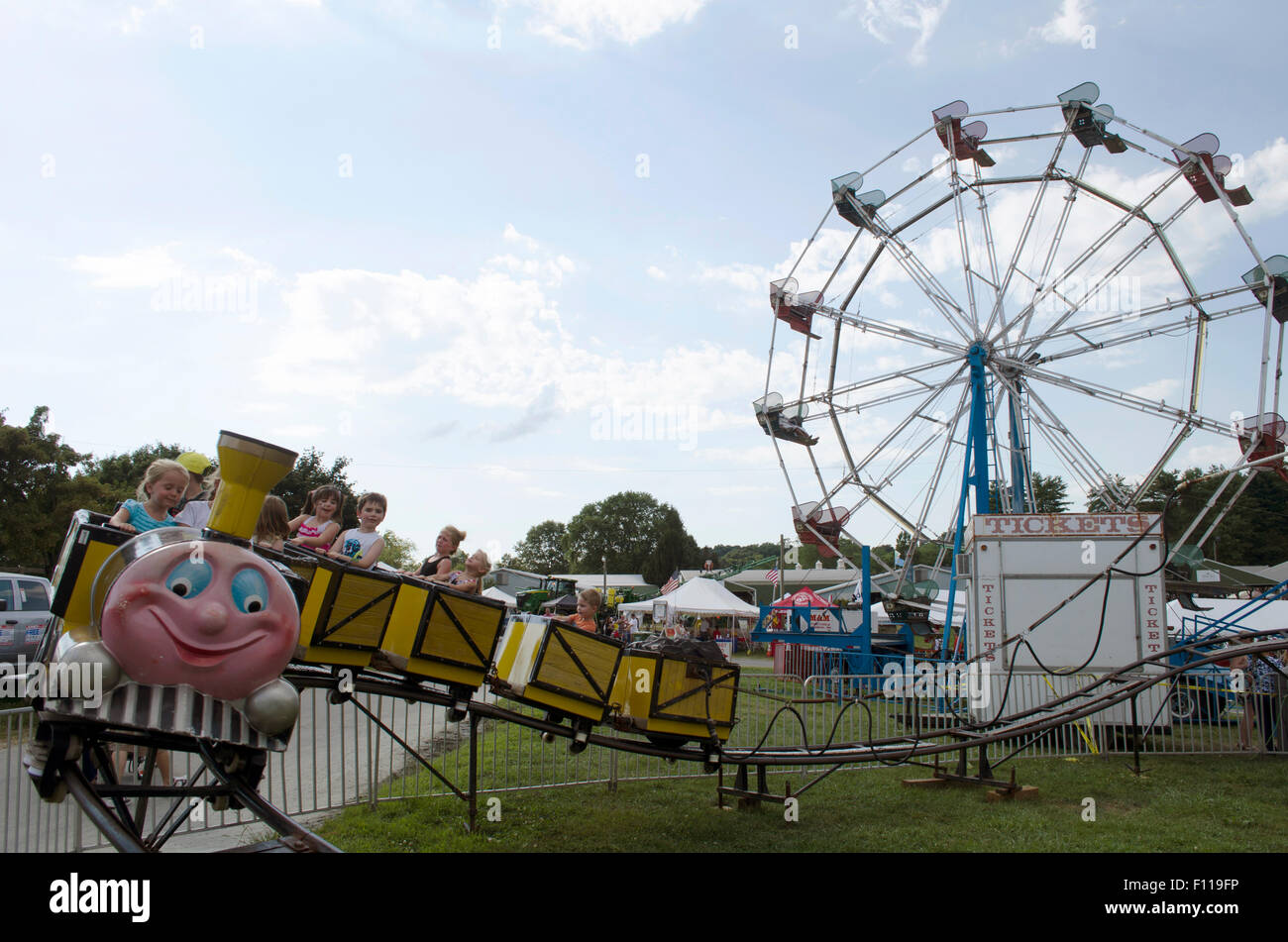 Kinder reiten ein Kiddy Ride im Jahrmarkt mit Riesenrad im Hintergrund Stockfoto