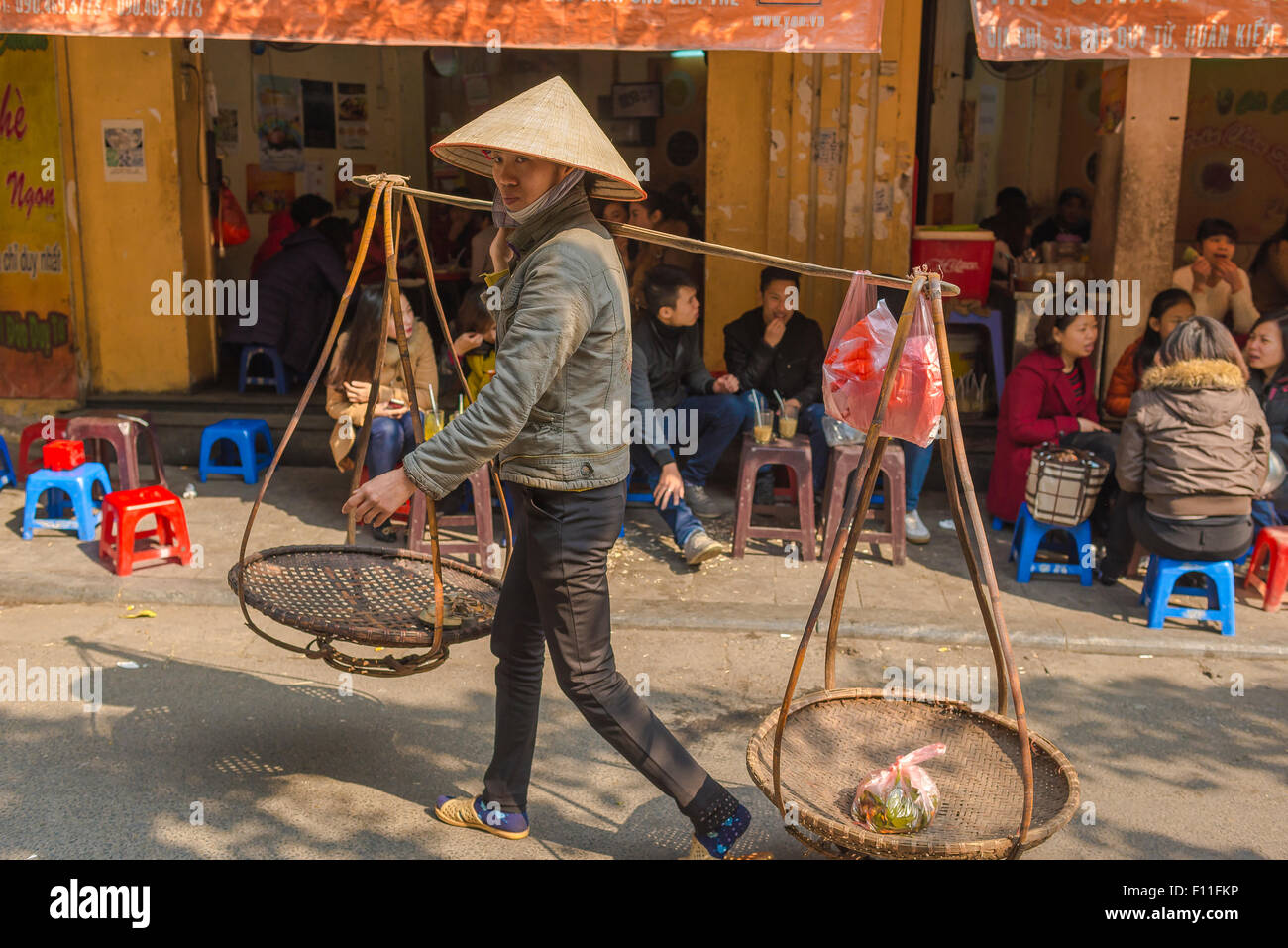 Vietnam Frau Vendor, ein Straßenhändler in einem kegelförmigen Hut trägt ihr Körbe durch die Altstadt von Hanoi, Vietnam. Stockfoto