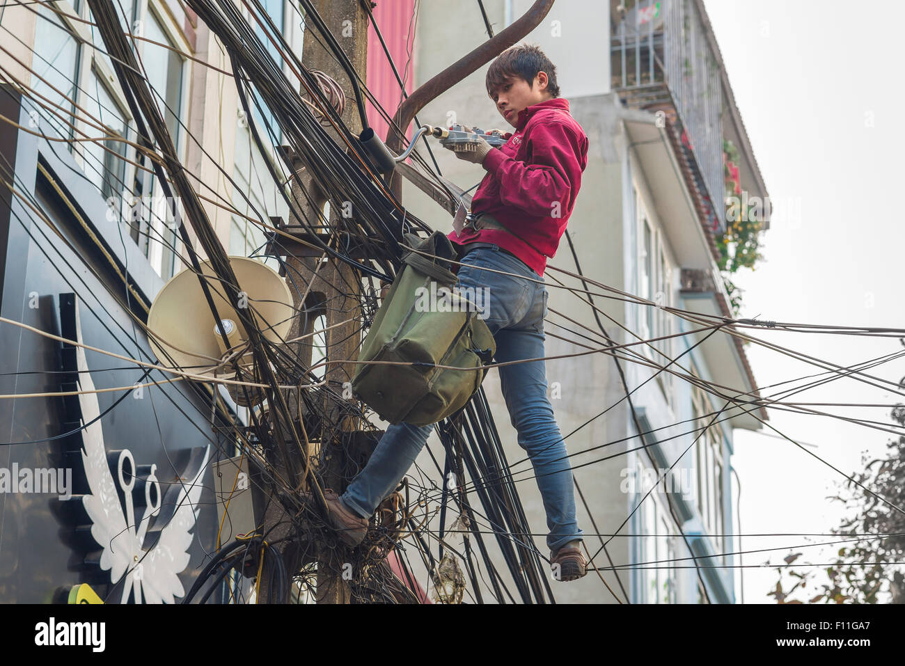 Vietnam Straße Kabel, oberhalb einer Straße im alten Viertel von Hanoi ein Elektroingenieur arbeitet unter einem dichten Gewirr von Stromleitungen, Vietnam Stockfoto