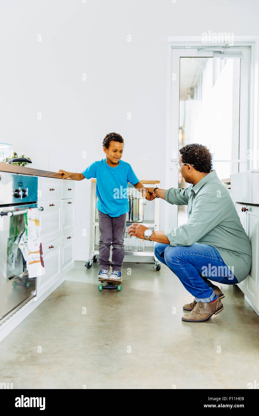 Vater Sohn Gleichgewicht auf Skateboard in der Küche zu helfen Stockfoto