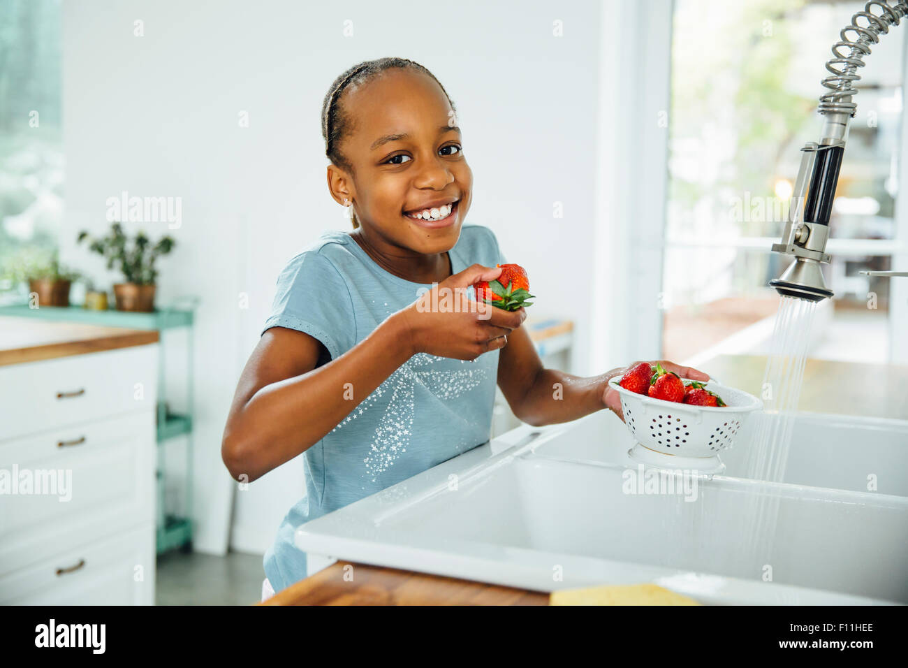 Schwarzes Mädchen essen Erdbeeren in Küche Stockfoto