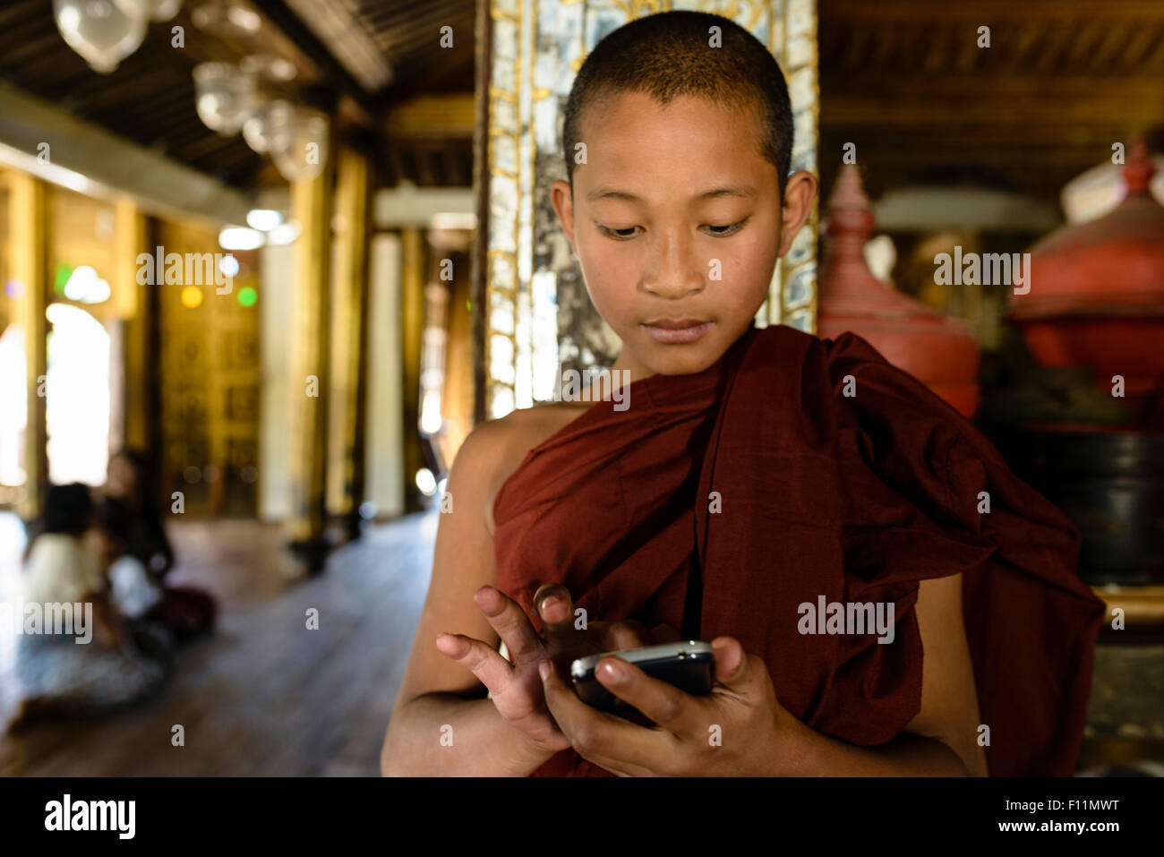 Asiatischer Mönch in der Ausbildung mit Handy im Innenbereich Stockfoto