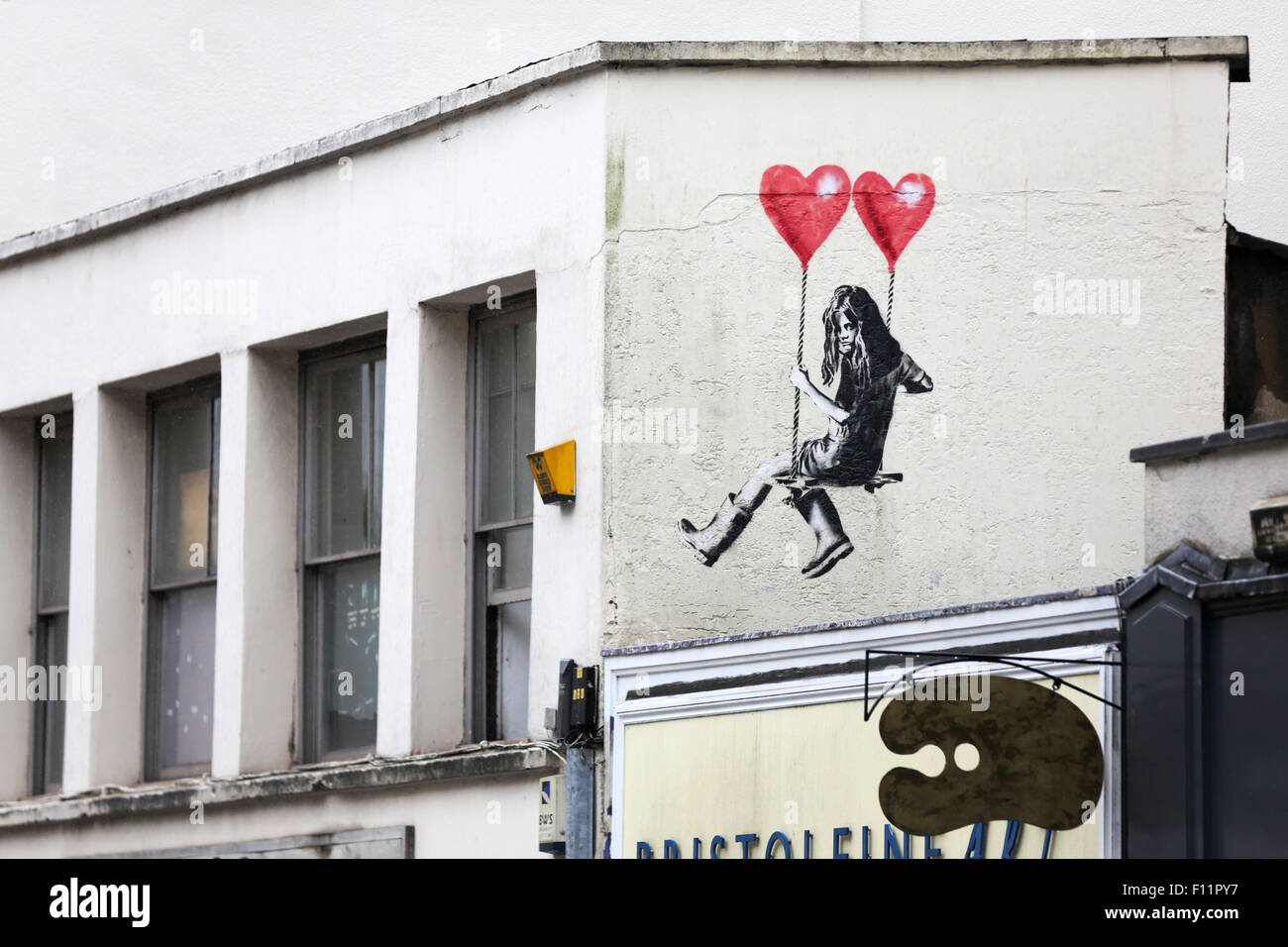 Street Art, Banksy-Stil, in Park Row Bristol. Das Bild zeigt ein Mädchen auf einer Frage, die von zwei herzförmigen Ballons aufgehängt wird. Der Künstler ist jps Stockfoto