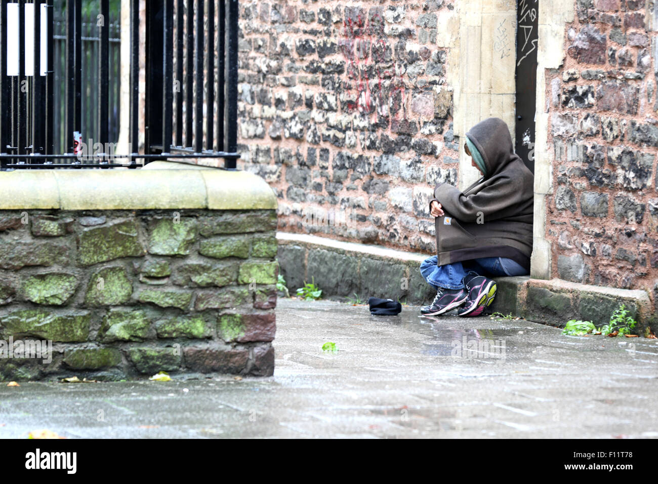 Eine weibliche Straße Bettler um Geld bitten auf einer nassen Straße der Stadt. Seine nassen kalten Tag und das Weibchen hat sich in zwei dicken Hoodies gewickelt Stockfoto