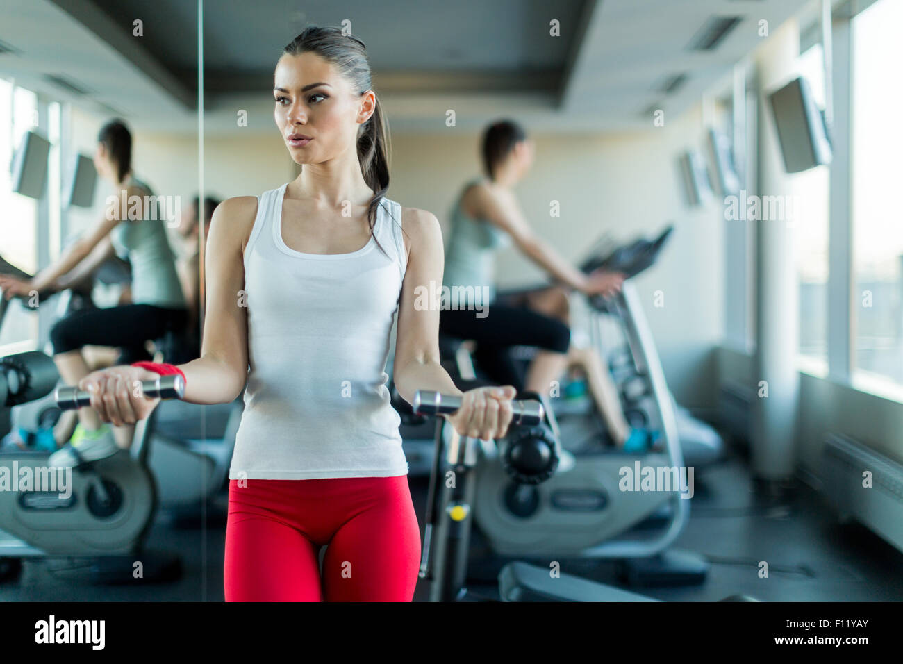 Schöne, junge Frau Heben von Gewichten im Fitnessstudio stehen neben einem Spiegel Stockfoto