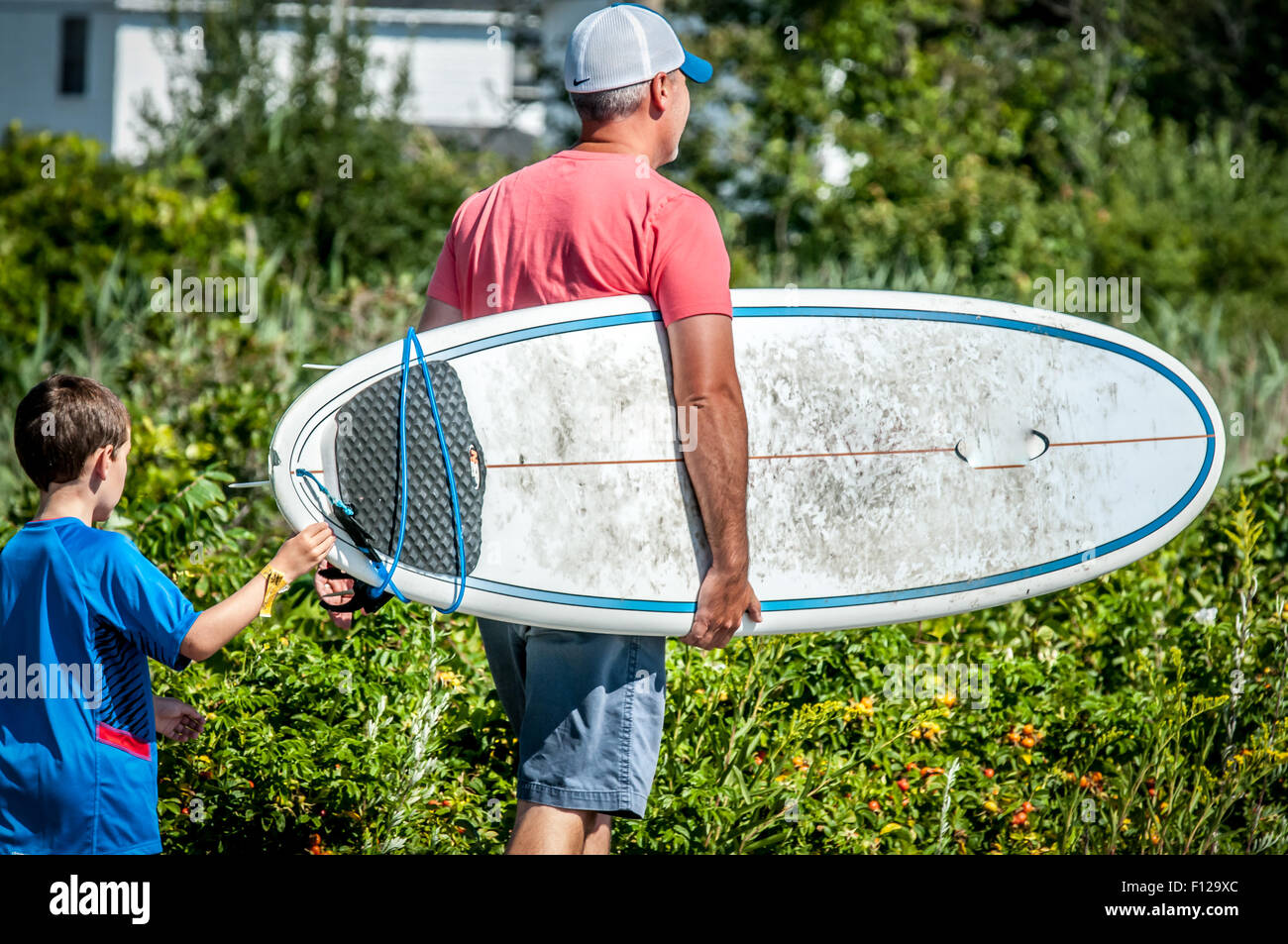 Auf der Suche nach Wellen, an einem schönen Sommertag diesen Vater und Sohn, Spaziergang durch die Stadt Straße mit einem Surfbrett, vielleicht auf der Suche nach Wellen Stockfoto