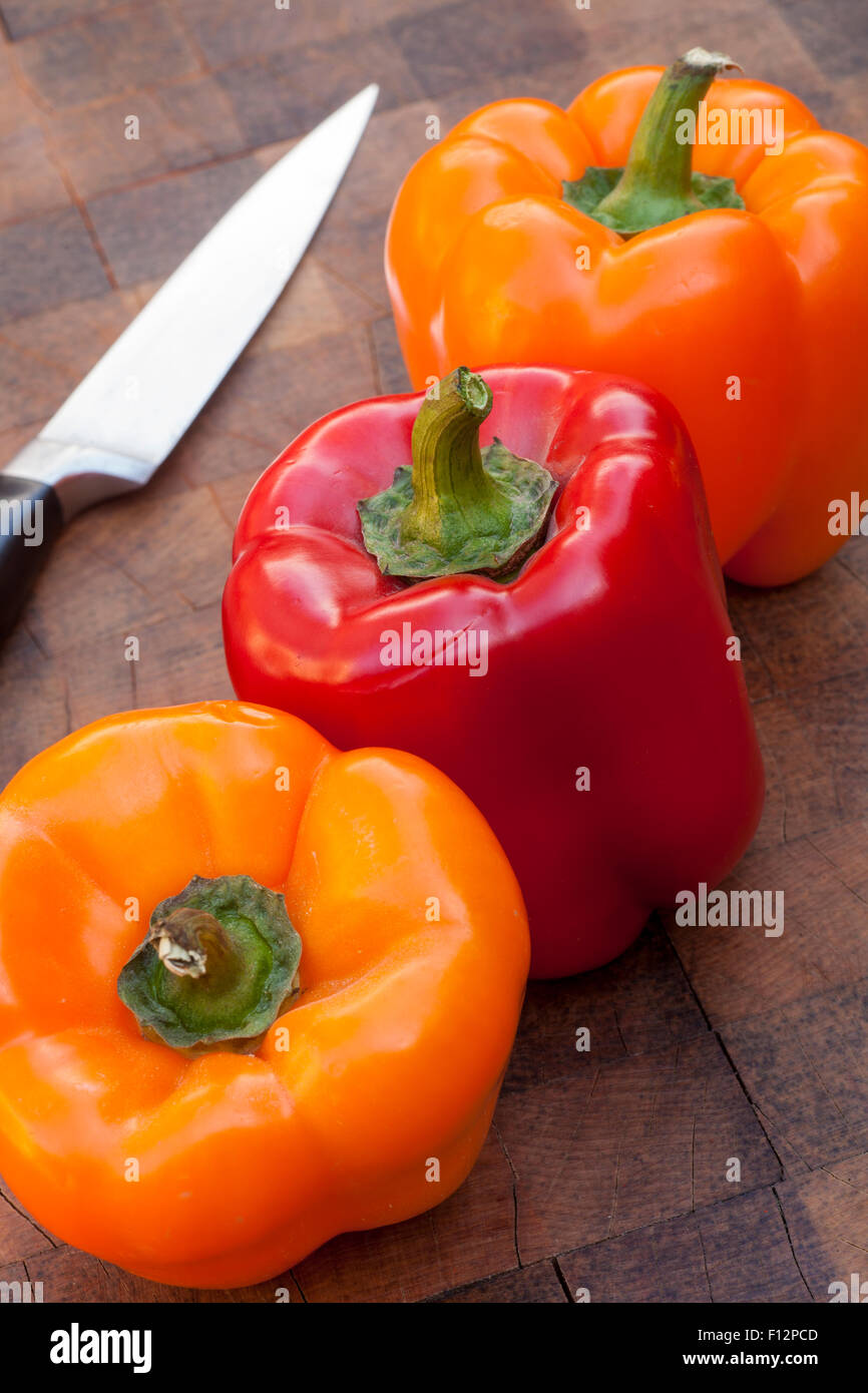 Bio rote und orange Paprika auf Schneidebrett mit einem Messer Stockfoto