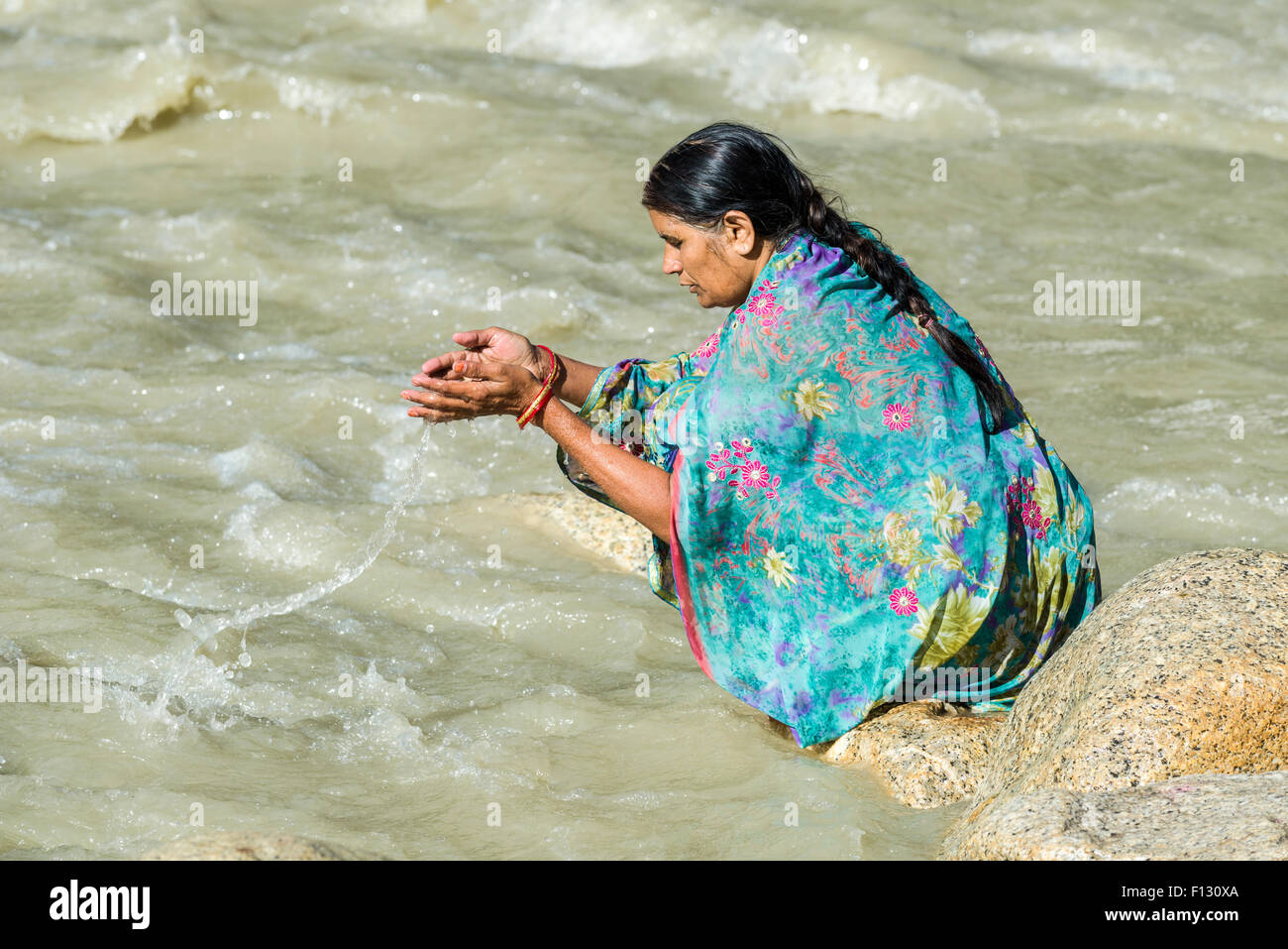 Ein weiblicher Pilger an den Ufern des Flusses Ganges betet mit Weihwasser, Gangotri, Uttarakhand, Indien, Stockfoto