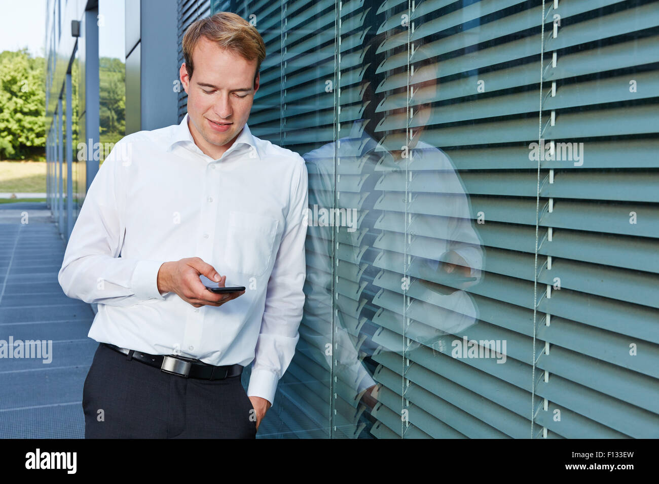 Business-Mann im Chat mit seinem Smartphone neben seinem Büro Stockfoto