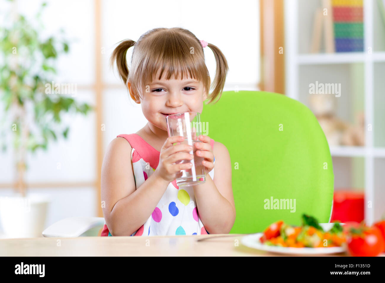 Lächelnde niedliche Mädchen hält Glas Wasser zu Hause Stockfoto