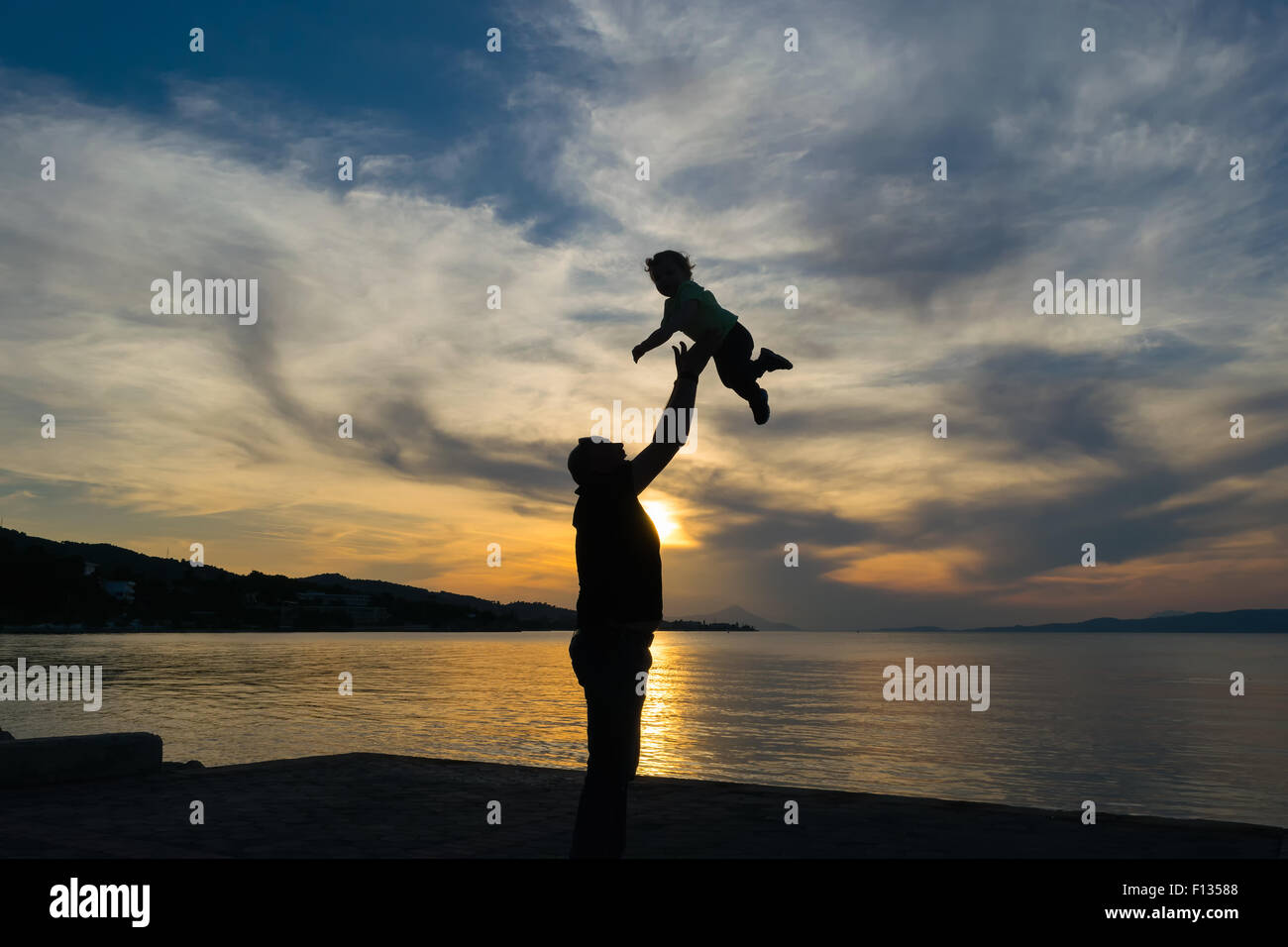 Silhouette eines Vaters und seines Sohnes gegen den Sonnenuntergang mit einem dramatischen Himmel. Stockfoto