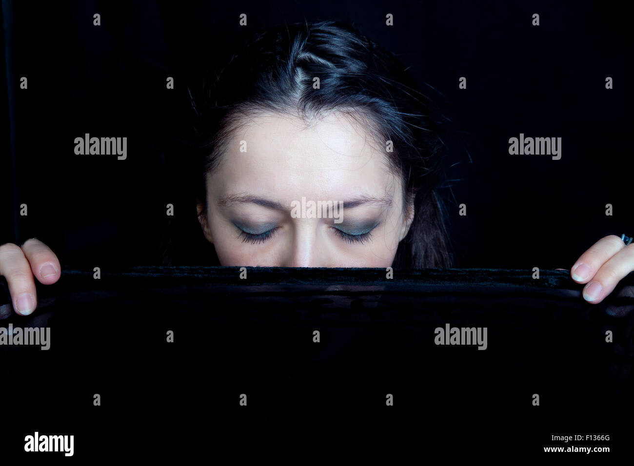 Frau mit ihren Augen geschlossen hält einen schwarzen Schleier vor ihrem Gesicht Stockfoto
