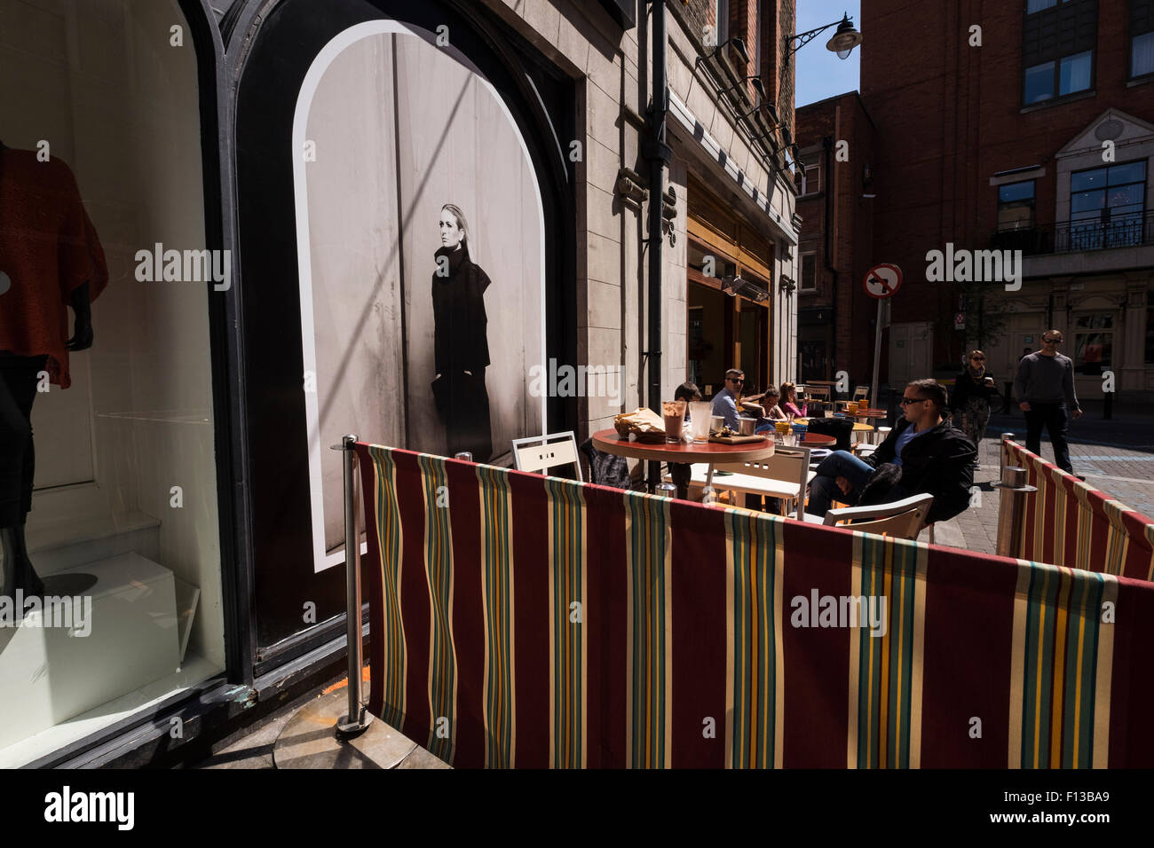 Straßenfotografie in Dublins Kreativquartier außerhalb Terrasse im Café, Bar mit Werbeplakat im Schaufenster, Trinker ein Stockfoto