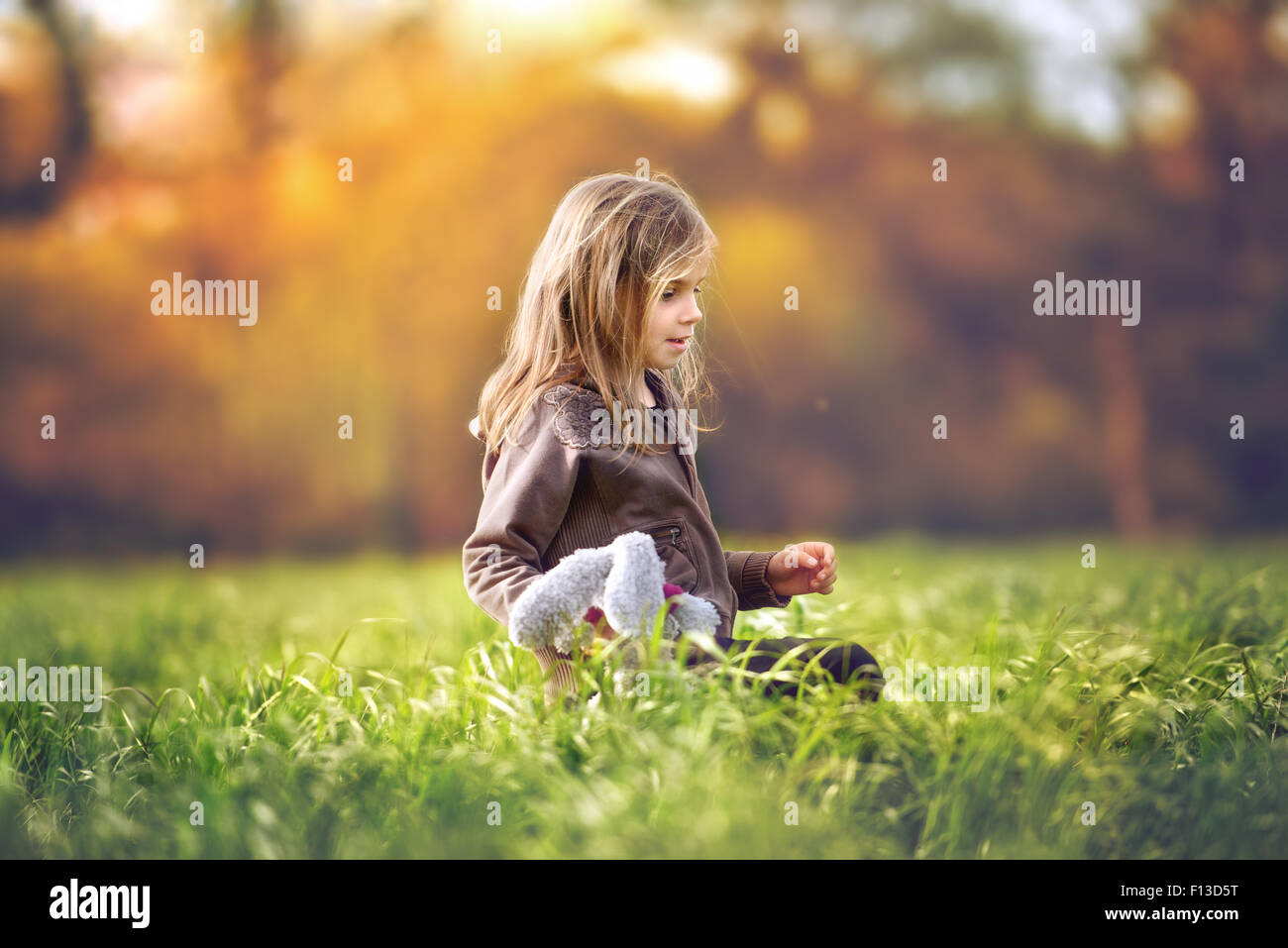 Mädchen sitzen in einem Feld mit einem Stofftier Stockfoto