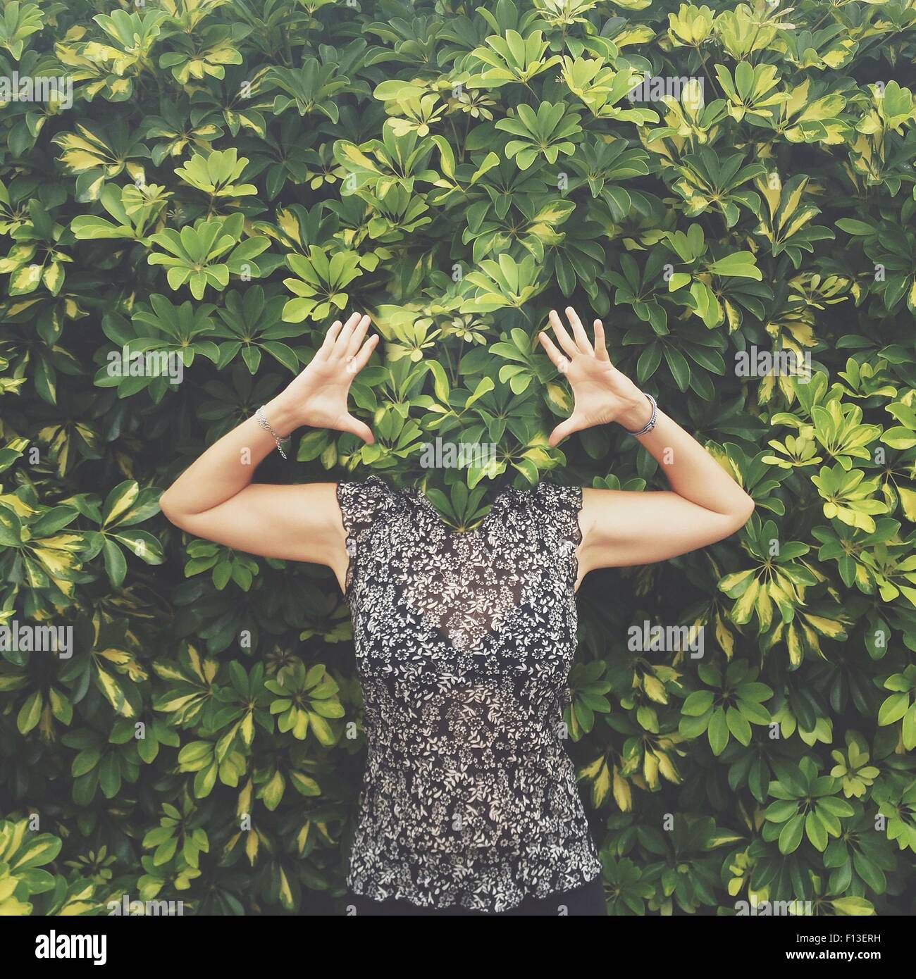 Frauen mit Gesicht versteckt hinter Blättern stehend mit erhobenen Armen Stockfoto