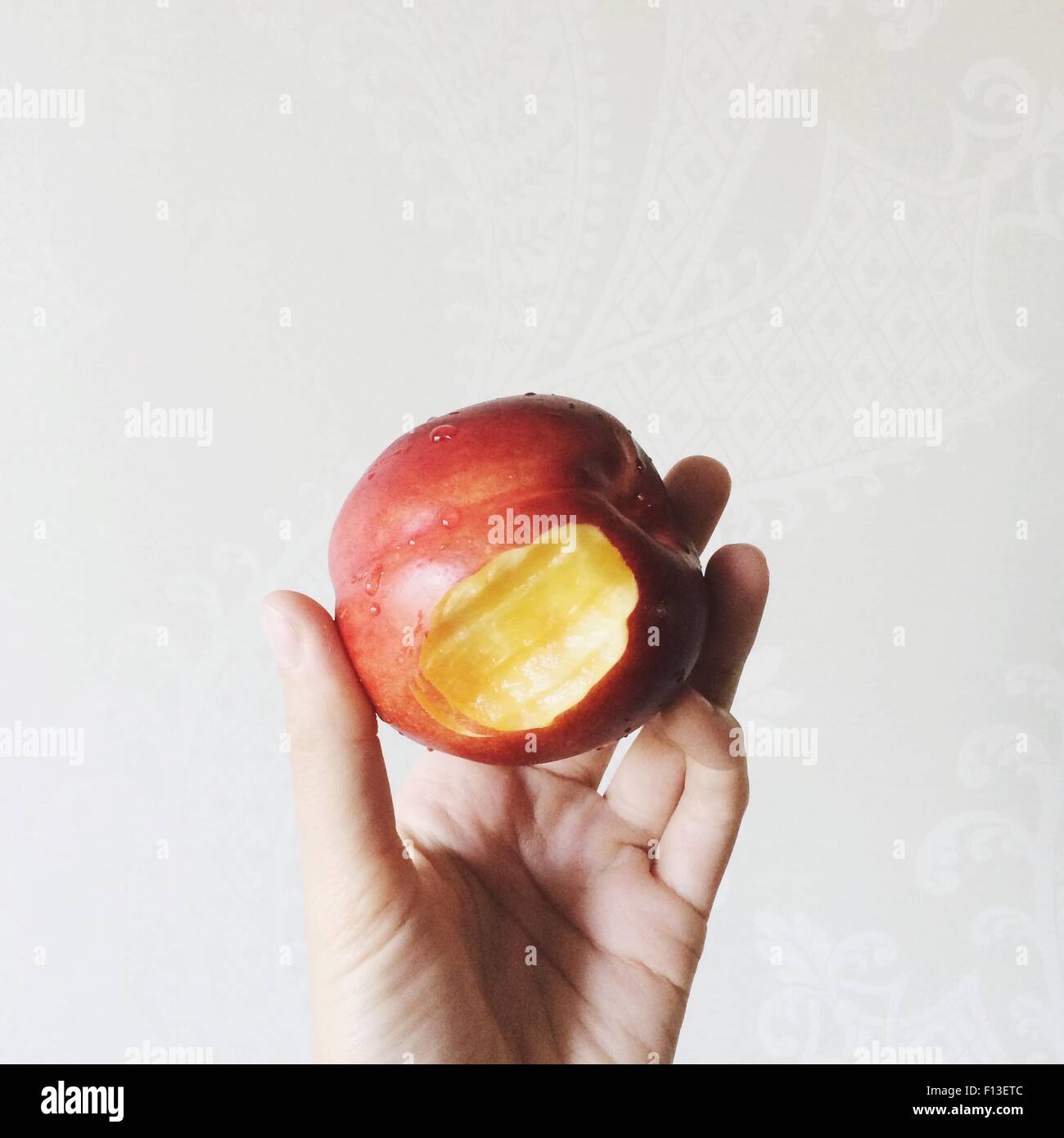 Hand hält einen Pfirsich mit einem Bisszeichen Stockfoto
