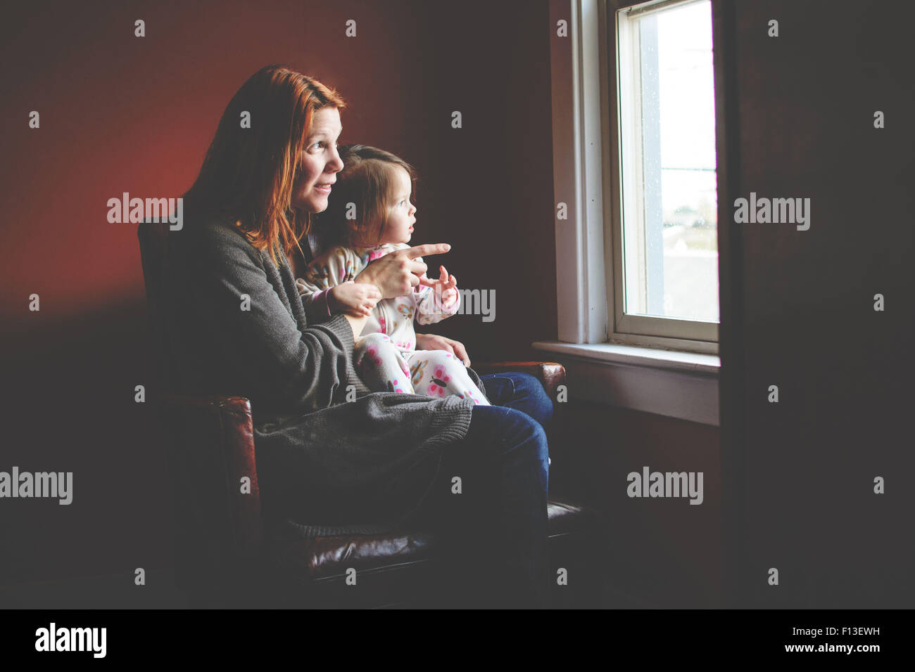 Babymädchen sitzen auf der Mutter Schoß, schaut aus dem Fenster Stockfoto