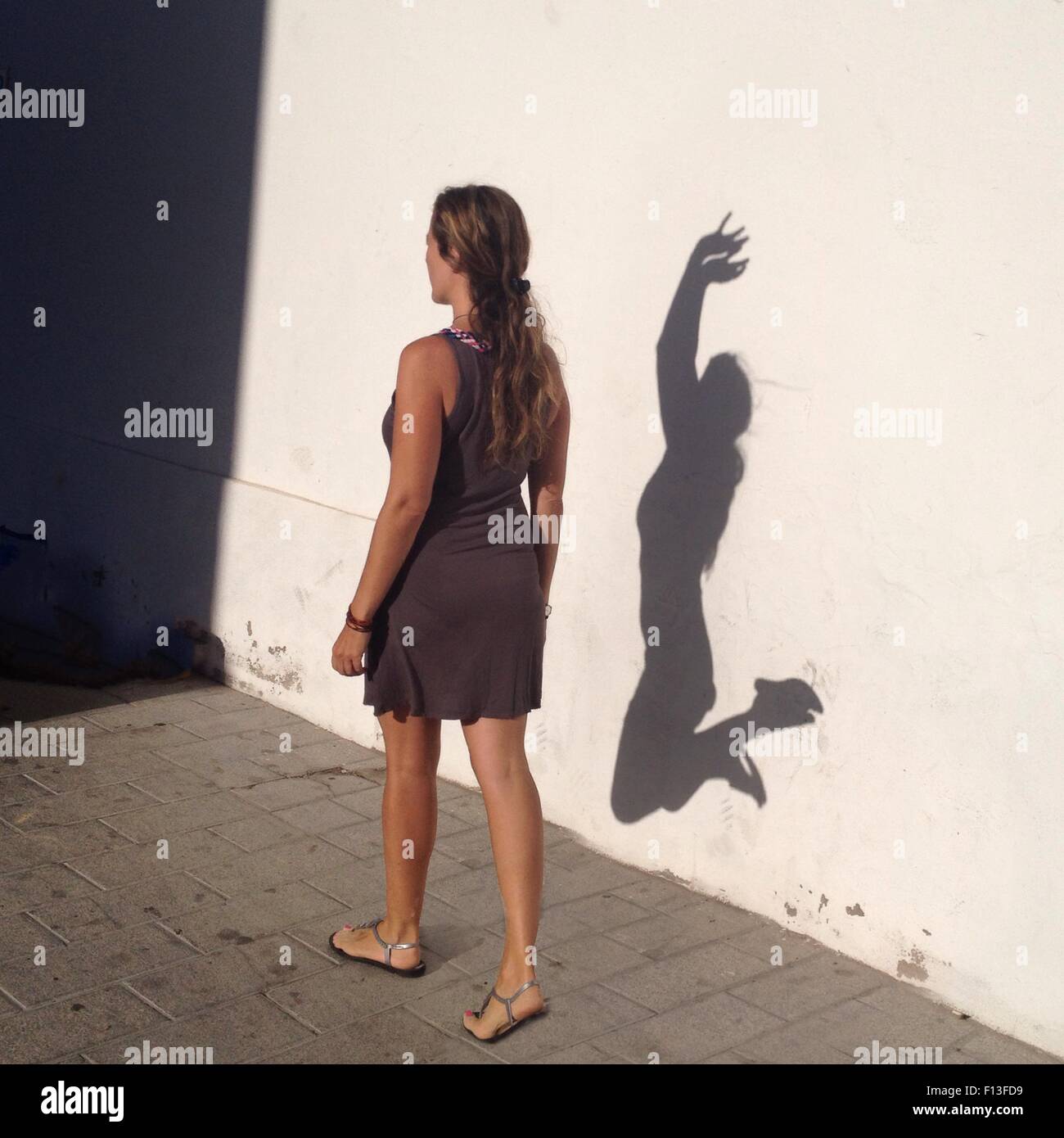 Frau, die an einer Wand vorbeigeht, mit ihrem Alter Ego Schatten, der vor Freude springt Stockfoto