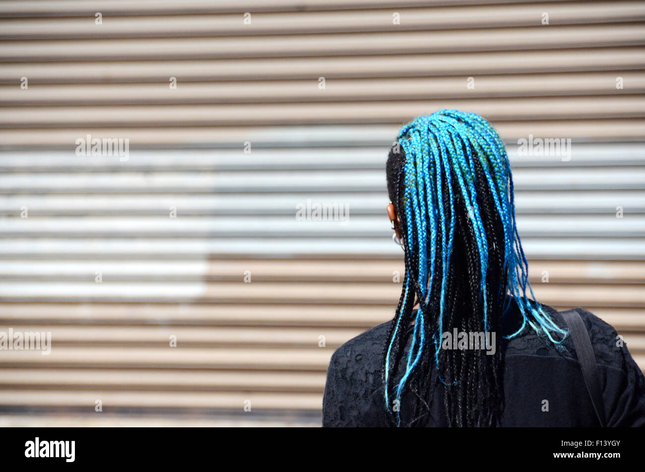 geflochtene blaue Haare schwarze Frau Ohr Telefone Knospen Straße Szene New York Usa Brooklyn Stockfoto