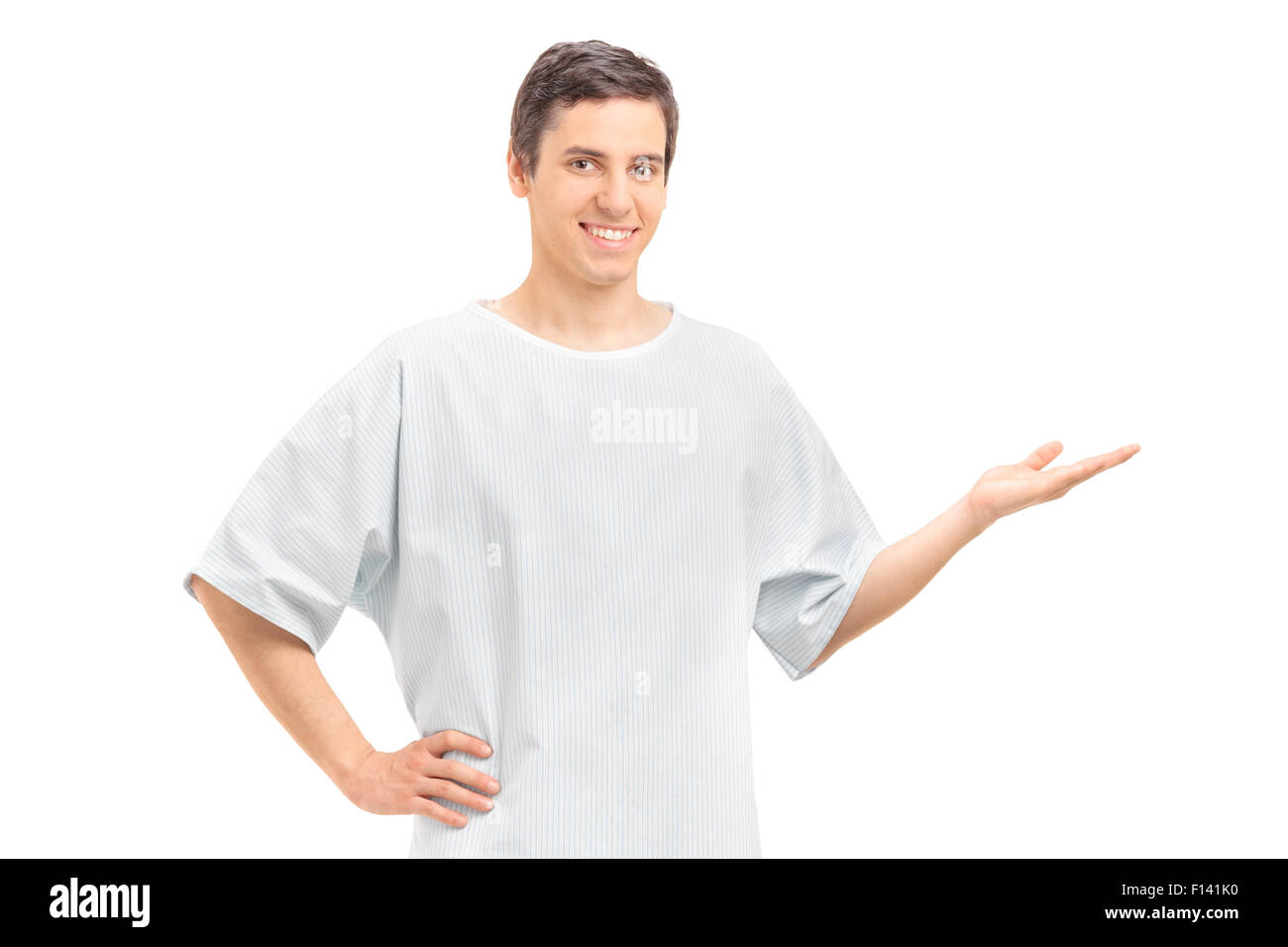 Junge männliche Patienten in einem Krankenhauskleid mit seiner Hand gestikulieren und schaut in die Kamera, die isoliert auf weißem Hintergrund Stockfoto