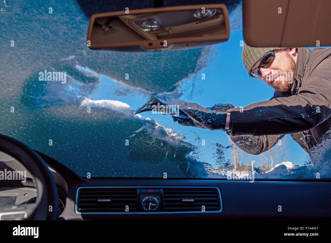 Reinigung Auto aus dem Schnee. Männer, die Reinigung der Windschutzscheibe von Schnee und Eis nach Schneesturm. Foto von im Inneren des Fahrzeugs. Stockfoto