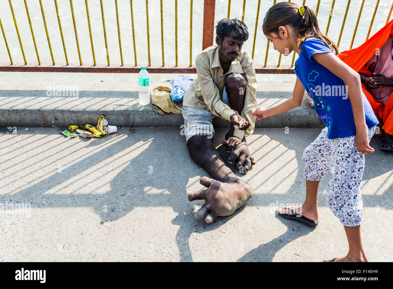 Ein Bettler mit Elephantiasis zu seinen Füßen empfängt etwas Geld von einem Mädchen an Harki Pauri Ghat am heiligen Fluss Ganges Stockfoto