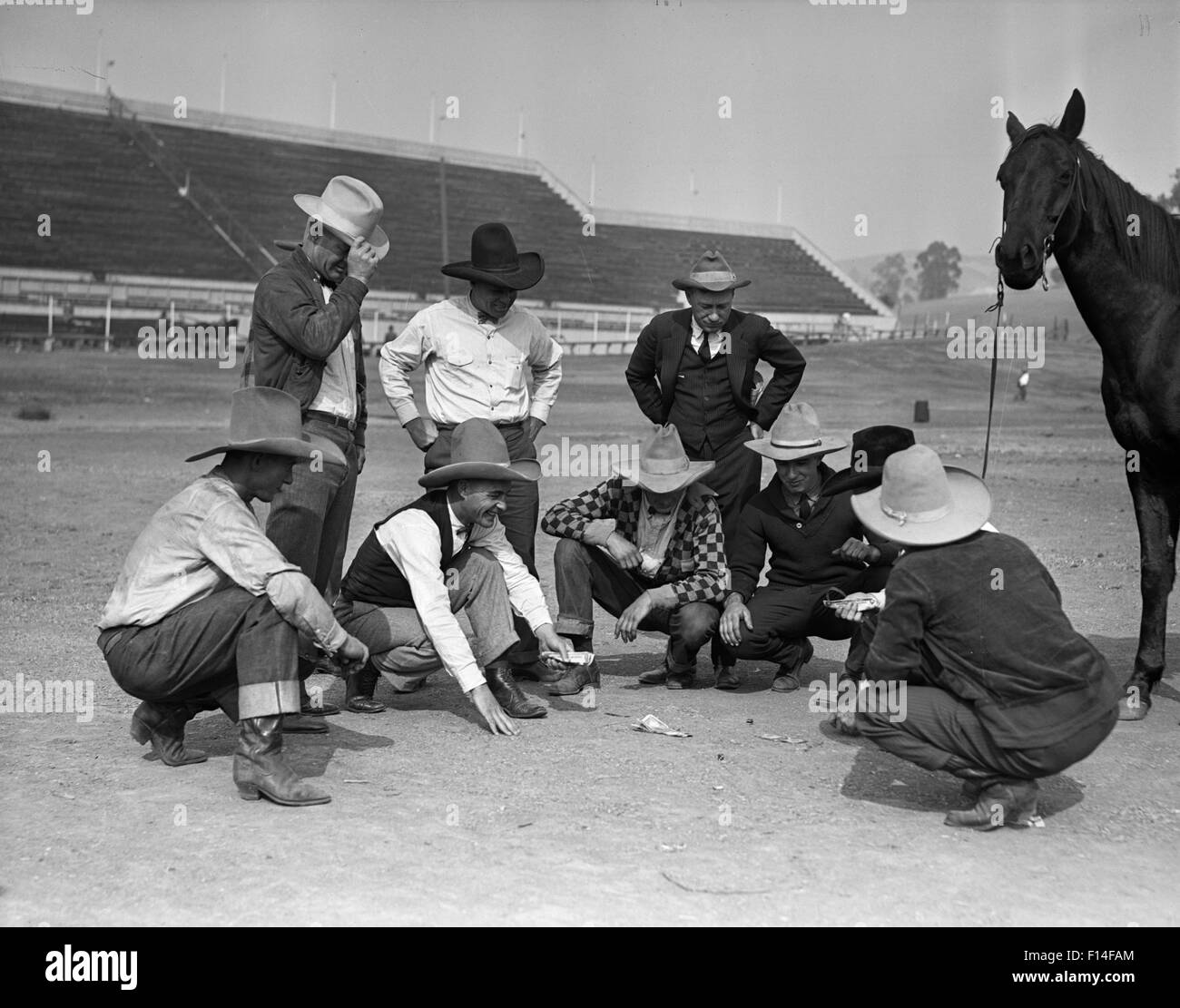 1930ER JAHRE GRUPPE MÄNNER COWBOYS MIT PFERD GLÜCKSSPIEL SPIELEN VON CRAPS AUS GRÜNDEN DER RENNSTRECKE RODEO ARENA Stockfoto