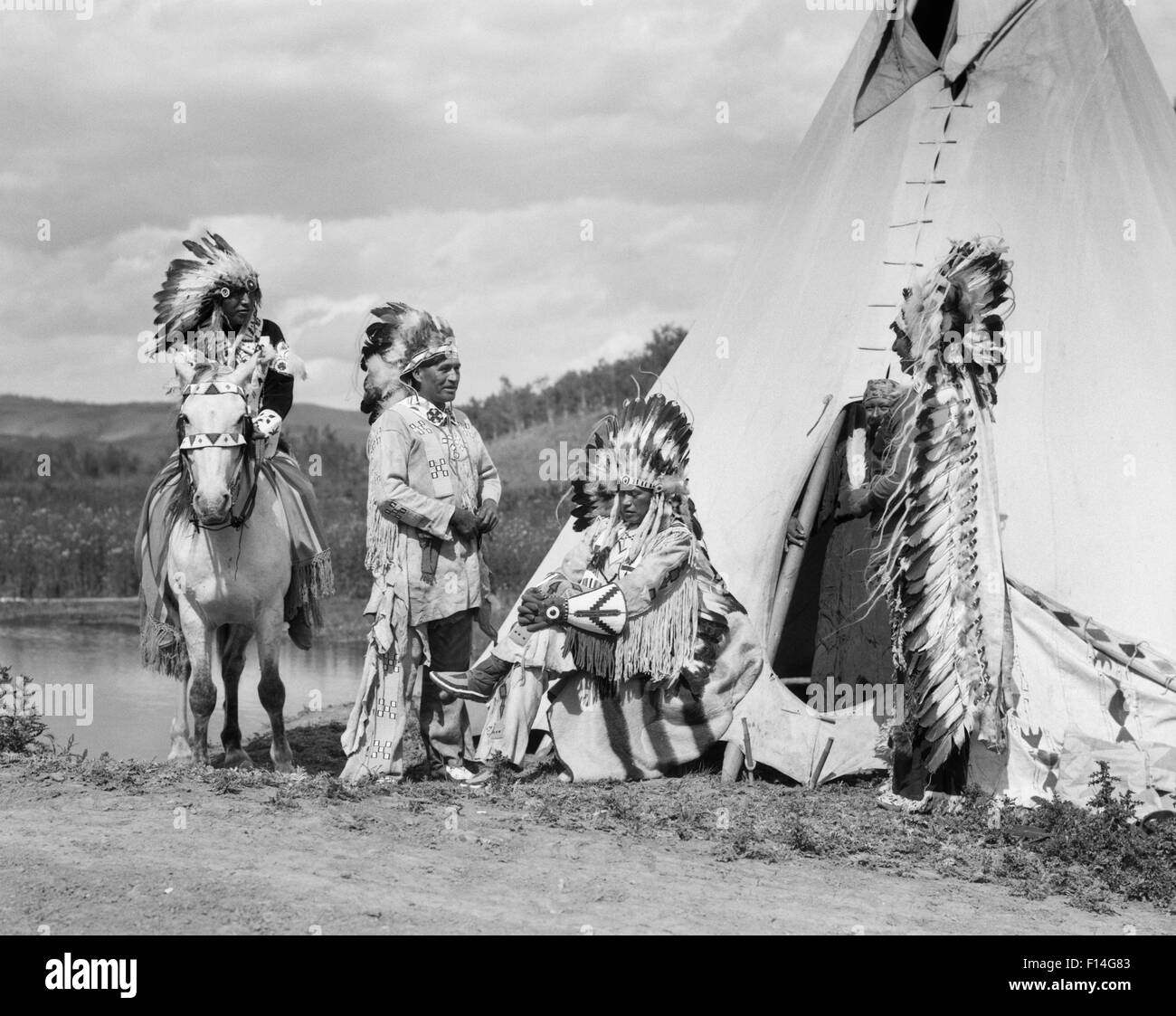 1920ER JAHREN VIER INDIANISCHEN STONEY SIOUX INDISCHE MÄNNER VERSAMMELT NEBEN TIPI TRAGEN VOLLE ADLER FEDER KRIEG MOTORHAUBEN ALBERTA KANADA Stockfoto